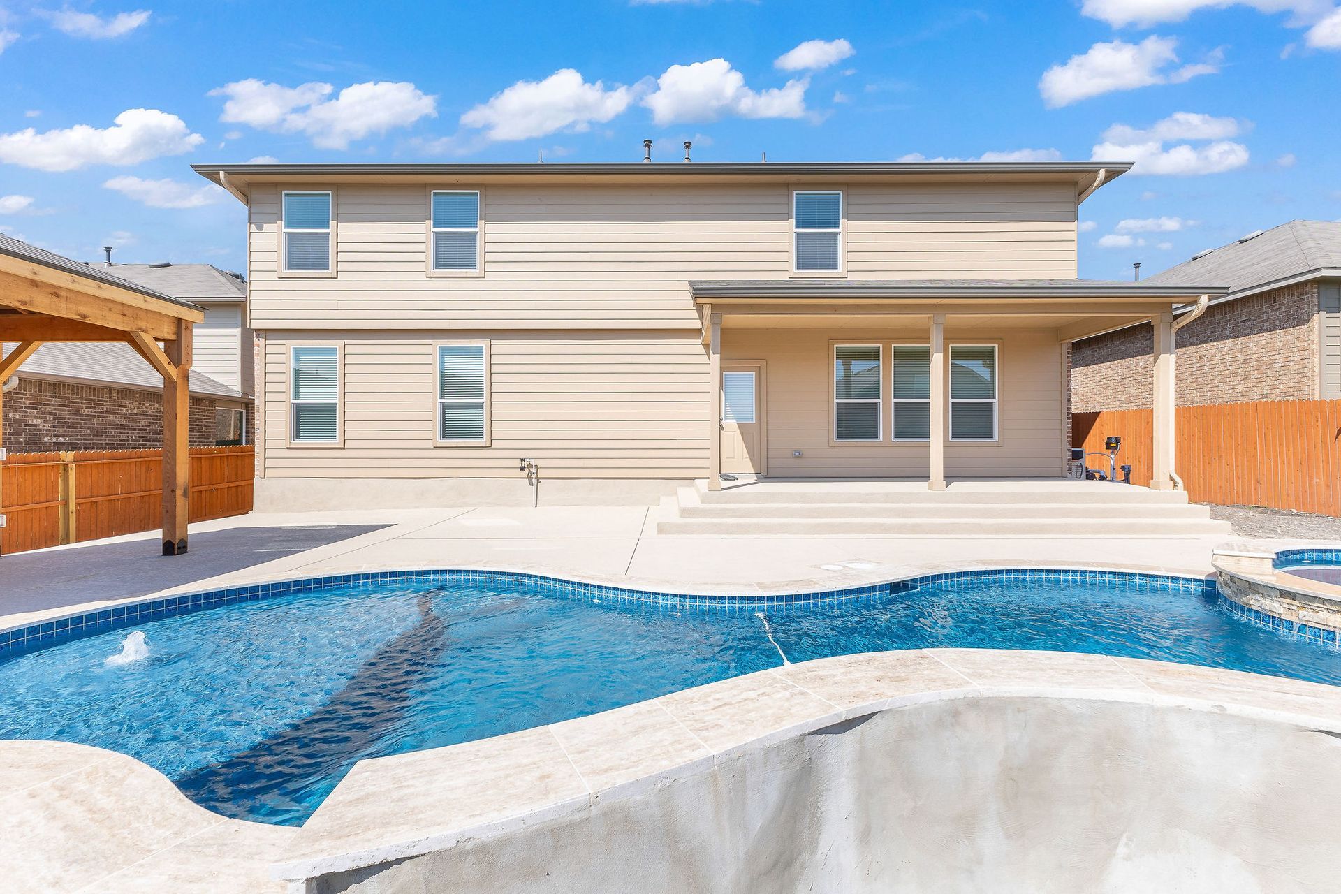 Modern backyard with a turquoise pool, lounge chairs, trees, and a sunset sky over hills.