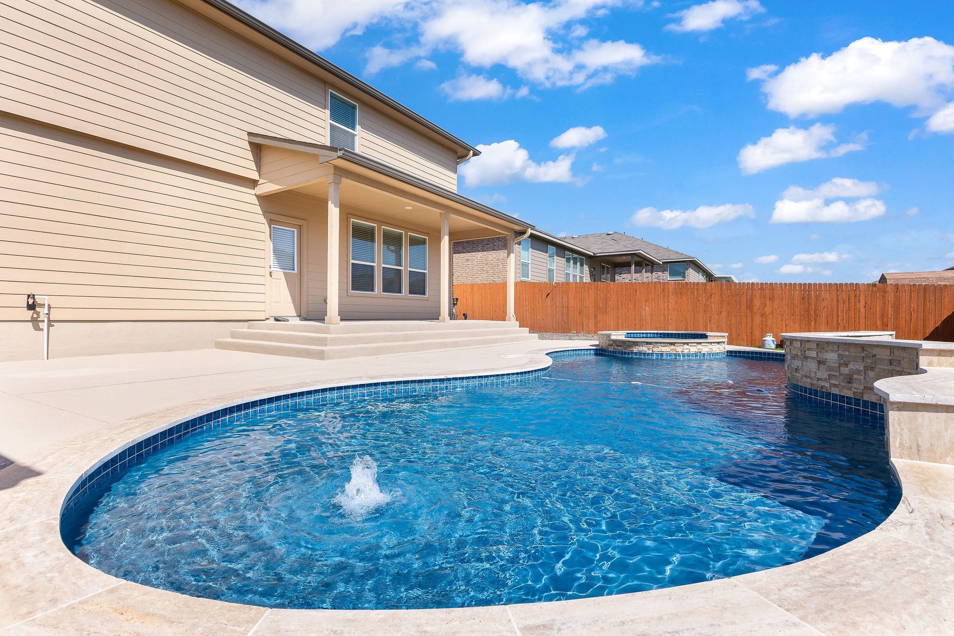 Modern backyard with a turquoise pool, lounge chairs, trees, and a sunset sky over hills.