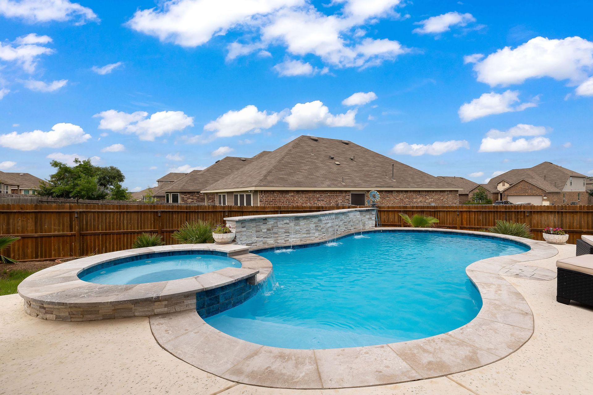 Backyard pool with blue water, hot tub, and stone waterfall under a partly cloudy sky