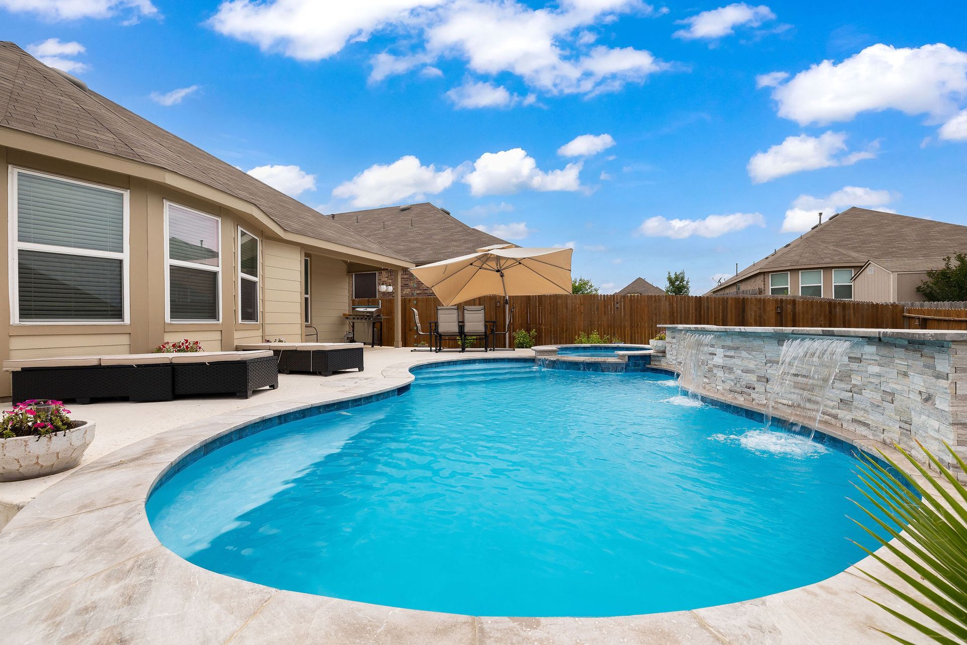 Backyard pool with spa, patio lounge chairs, and desert-style homes under a bright blue sky