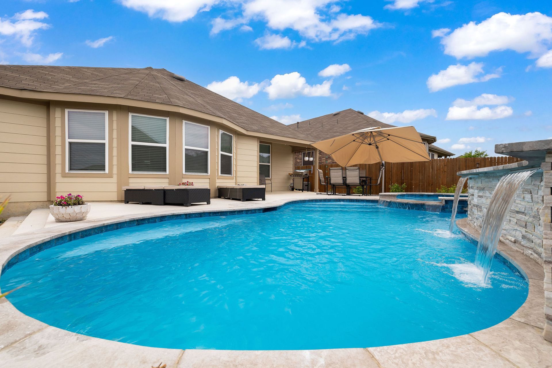 Backyard pool with spa, patio lounge chairs, and desert-style homes under a bright blue sky
