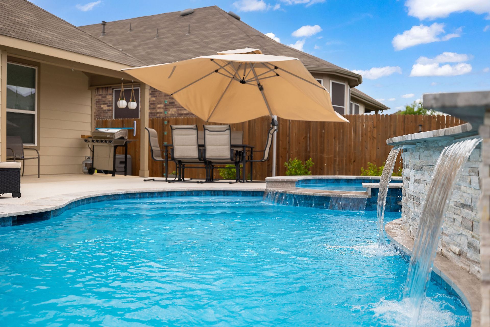 Backyard pool with spa, patio lounge chairs, and desert-style homes under a bright blue sky