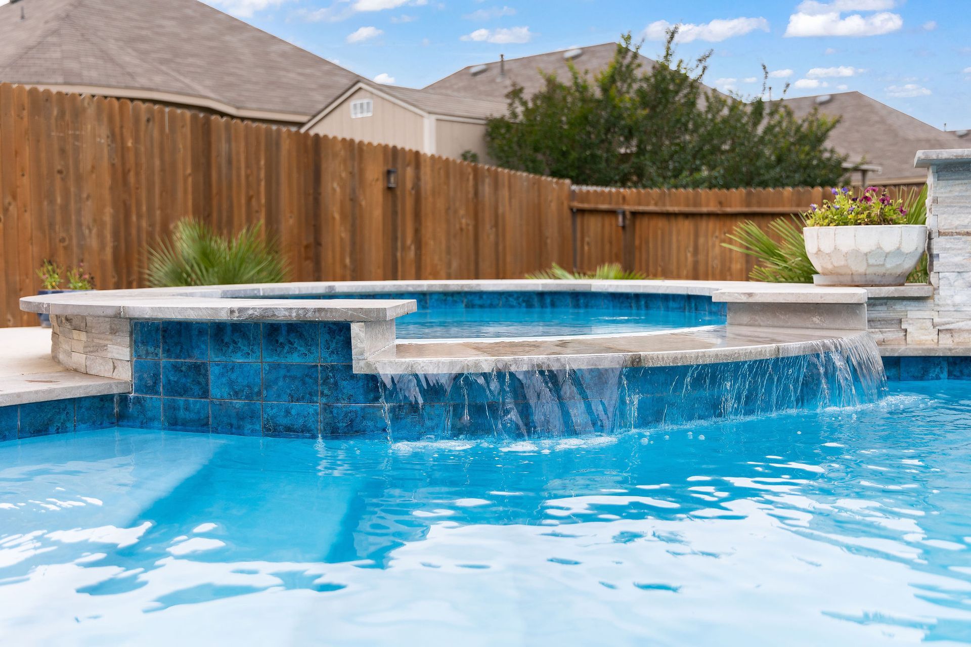 Backyard pool with spa, patio lounge chairs, and desert-style homes under a bright blue sky