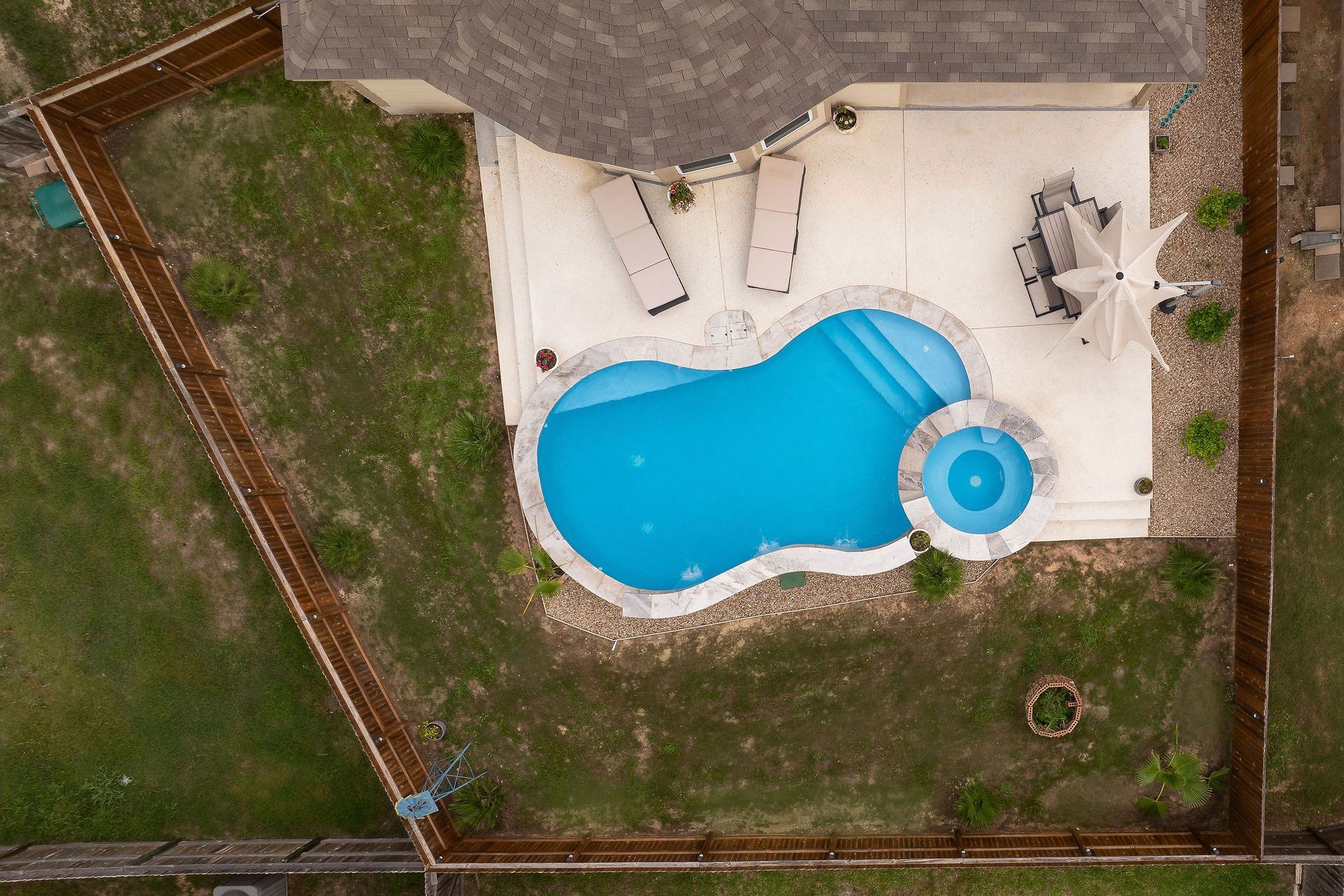 Backyard pool with spa, patio lounge chairs, and desert-style homes under a bright blue sky