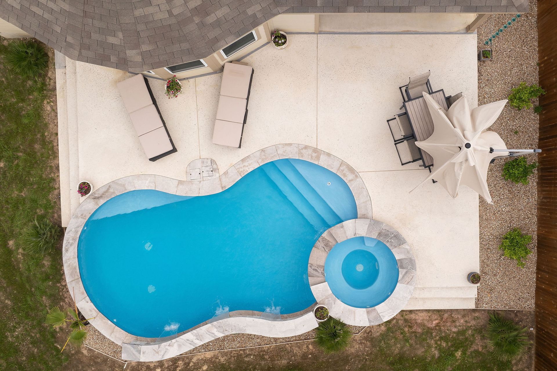 Backyard pool with spa, patio lounge chairs, and desert-style homes under a bright blue sky