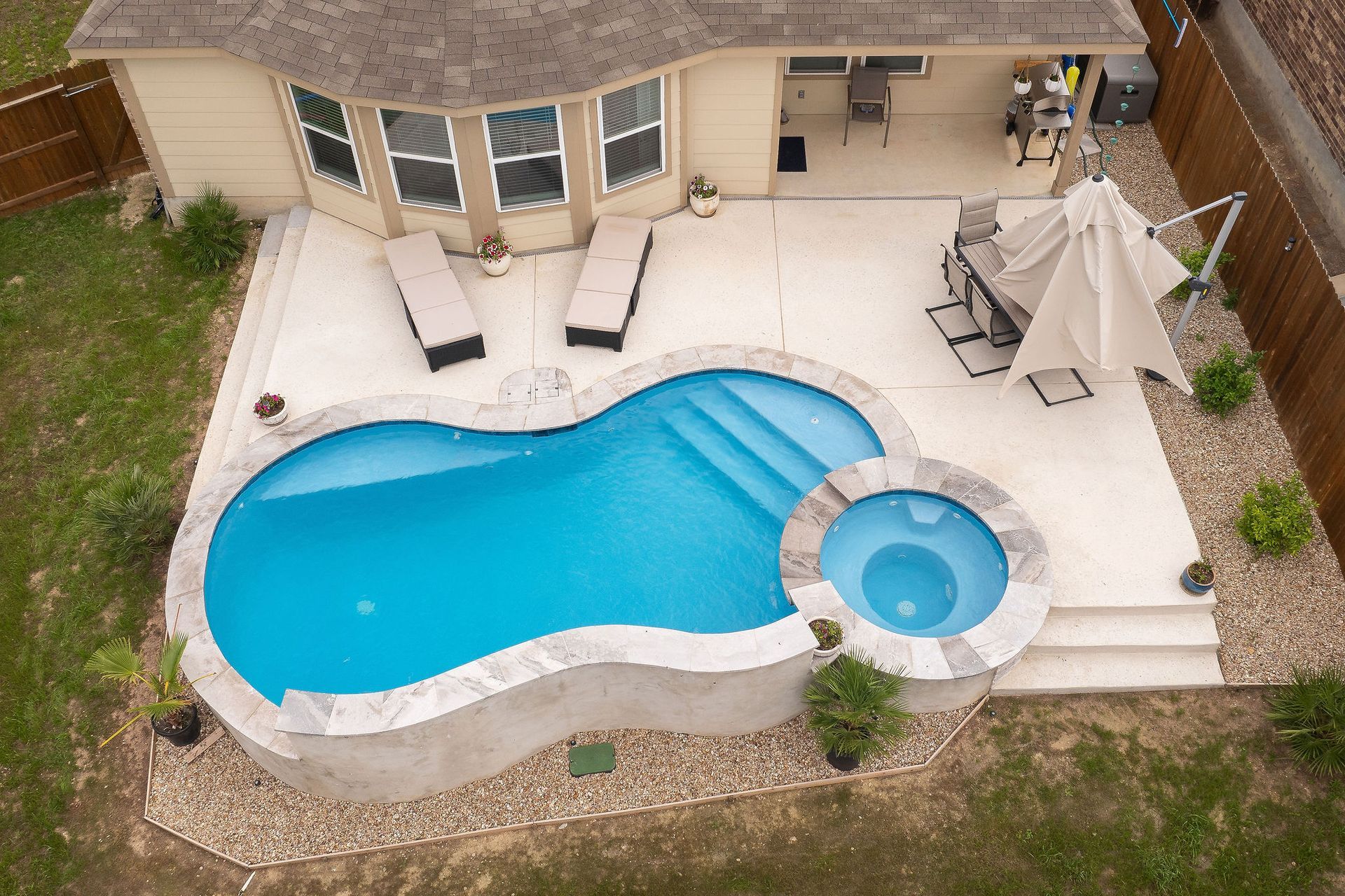 Backyard pool with spa, patio lounge chairs, and desert-style homes under a bright blue sky