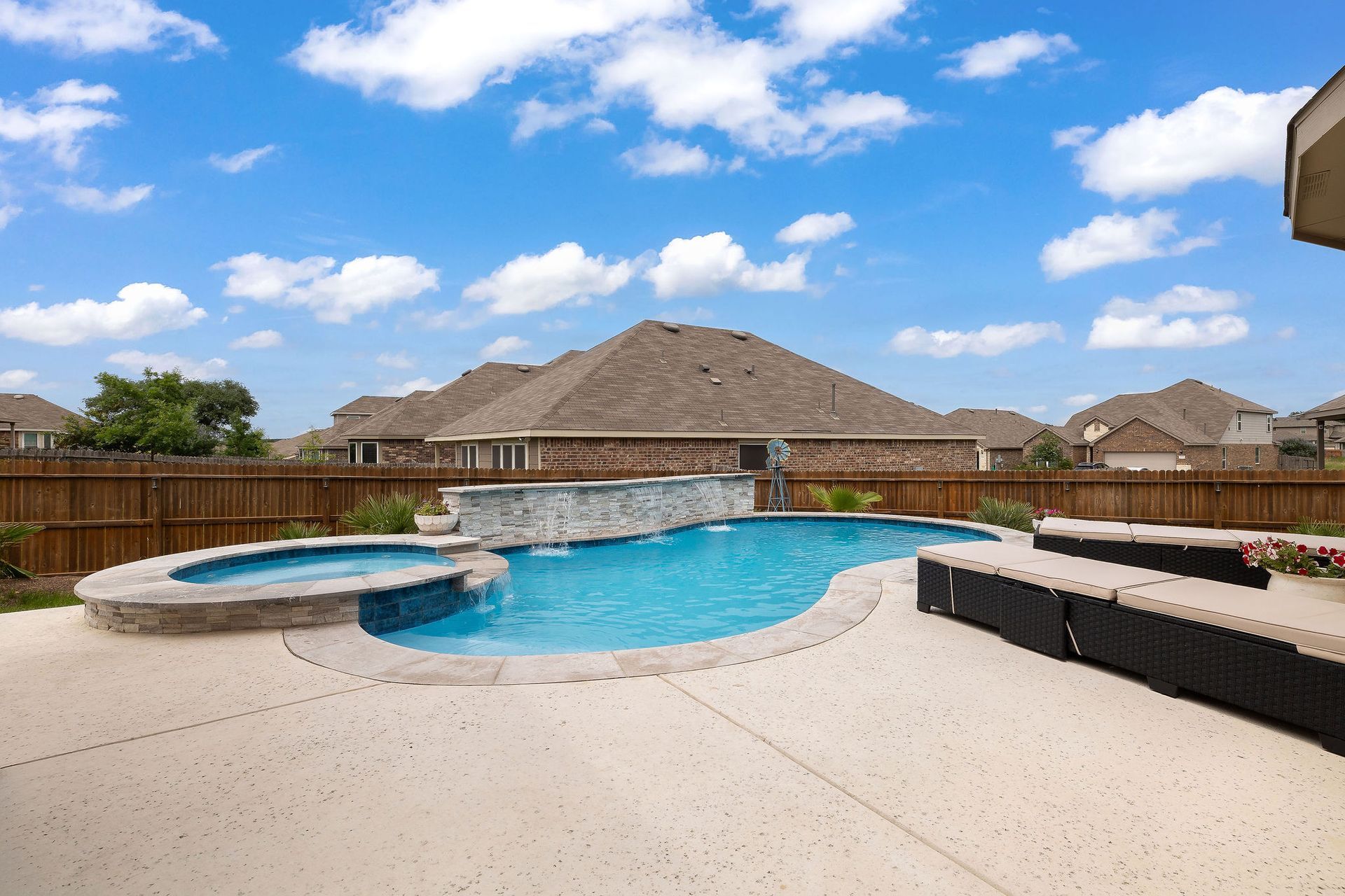 Backyard pool with spa, patio lounge chairs, and desert-style homes under a bright blue sky