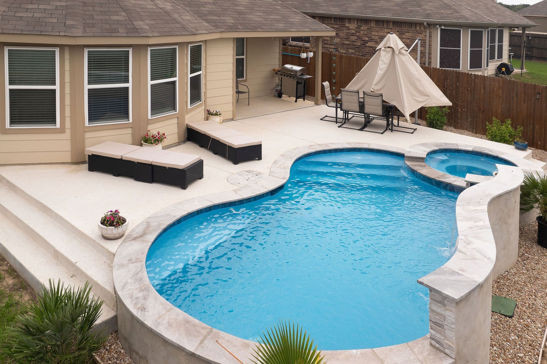 Backyard pool with spa, patio lounge chairs, and desert-style homes under a bright blue sky