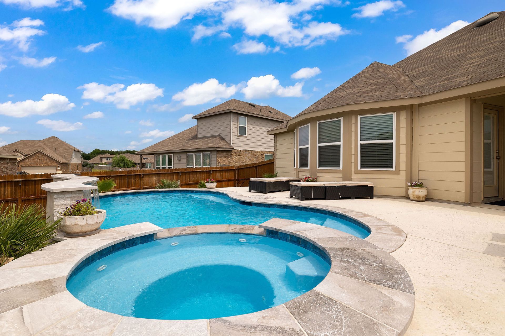 Backyard with a swimming pool, hot tub, and patio beside a suburban house under a blue sky
