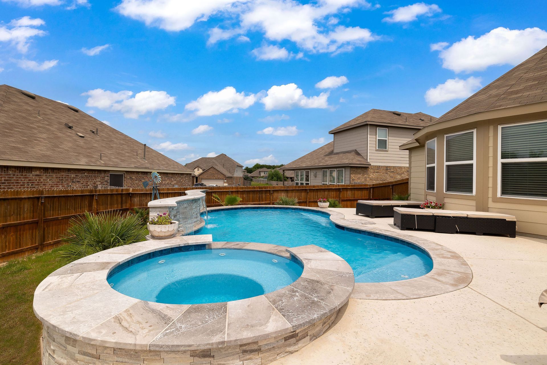 Backyard pool with spa, patio lounge chairs, and desert-style homes under a bright blue sky