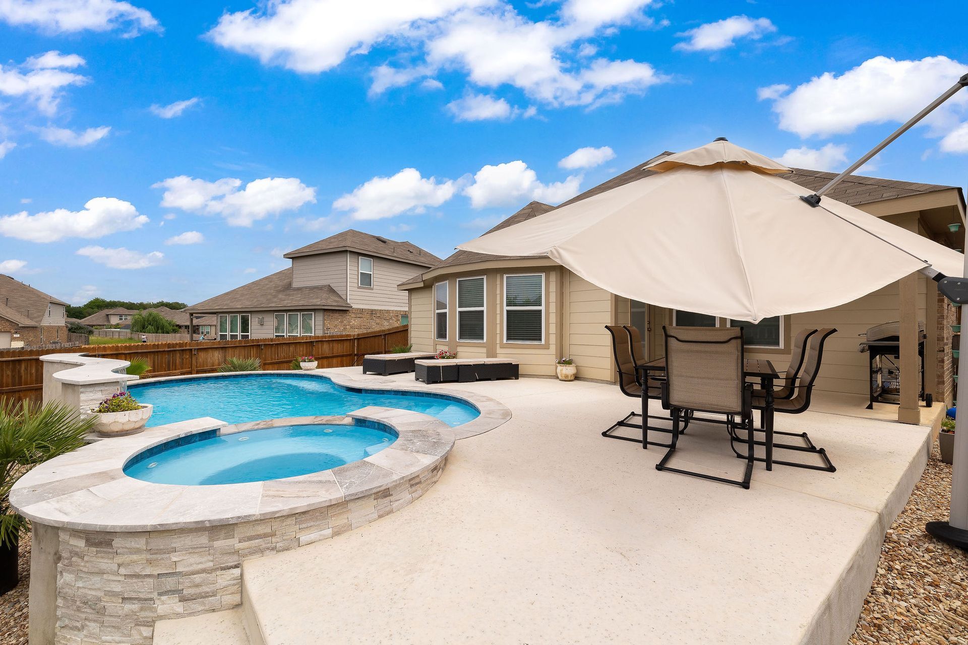 Backyard pool with spa, patio lounge chairs, and desert-style homes under a bright blue sky