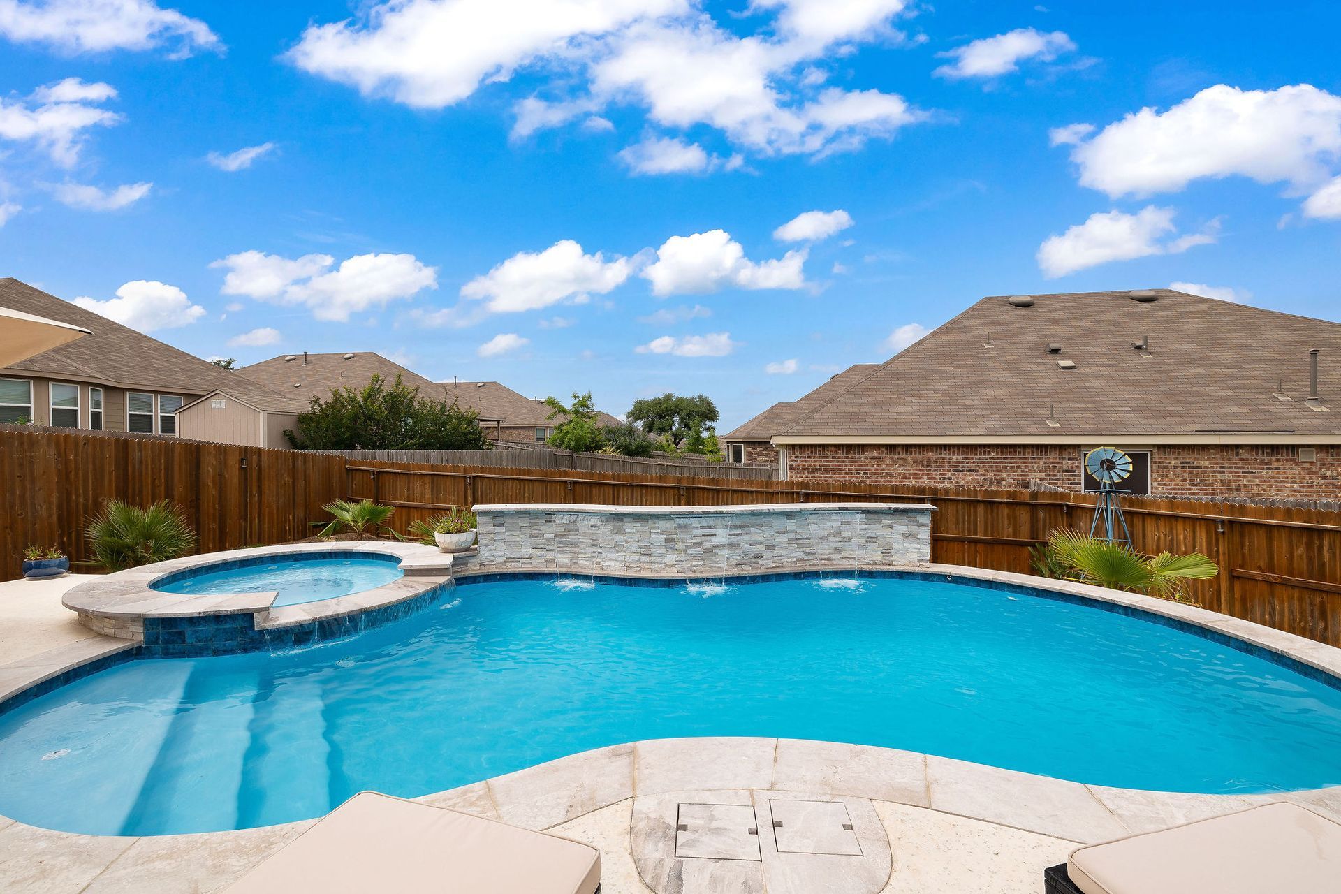 Backyard pool with spa, patio lounge chairs, and desert-style homes under a bright blue sky