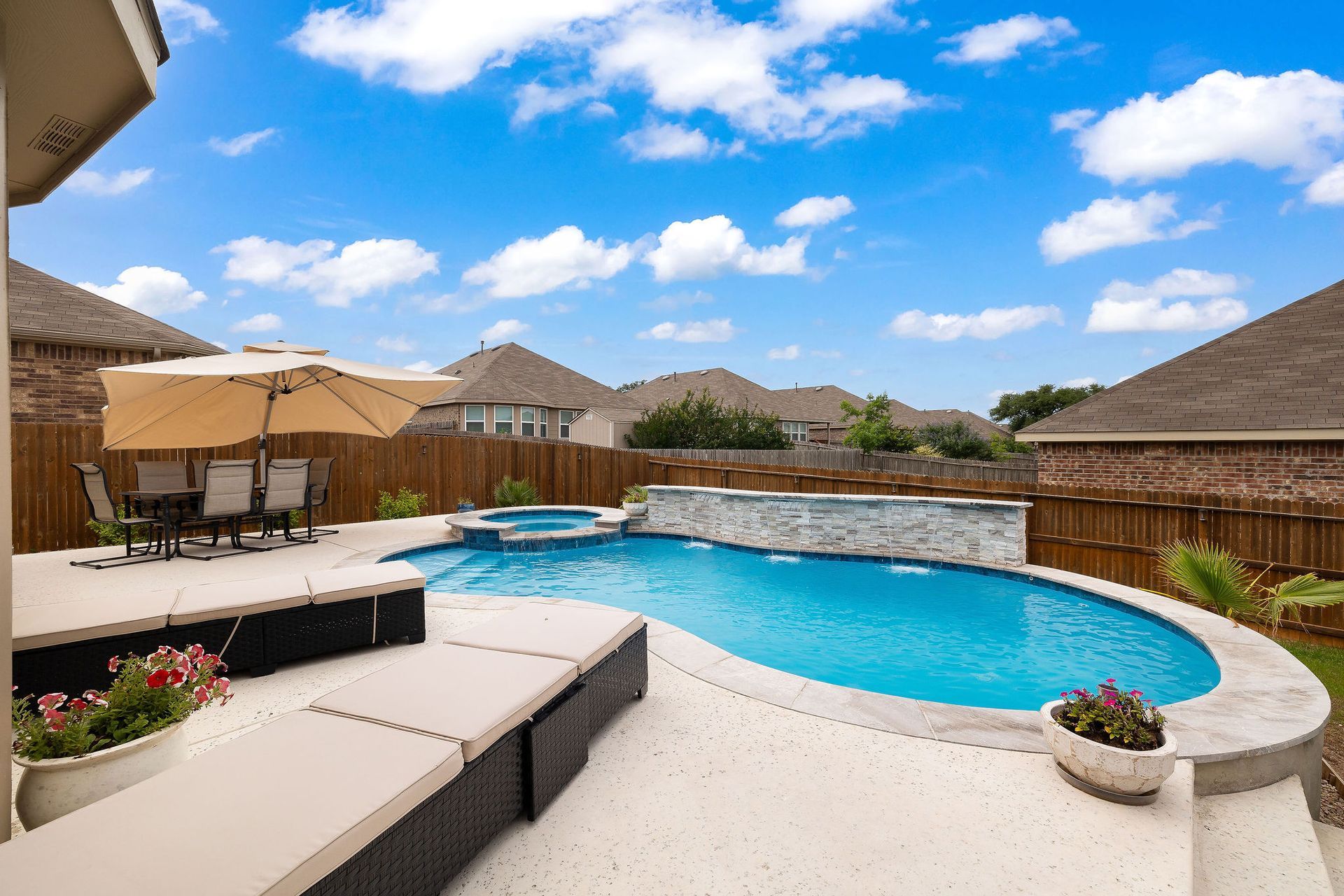 Backyard pool with spa, patio lounge chairs, and desert-style homes under a bright blue sky