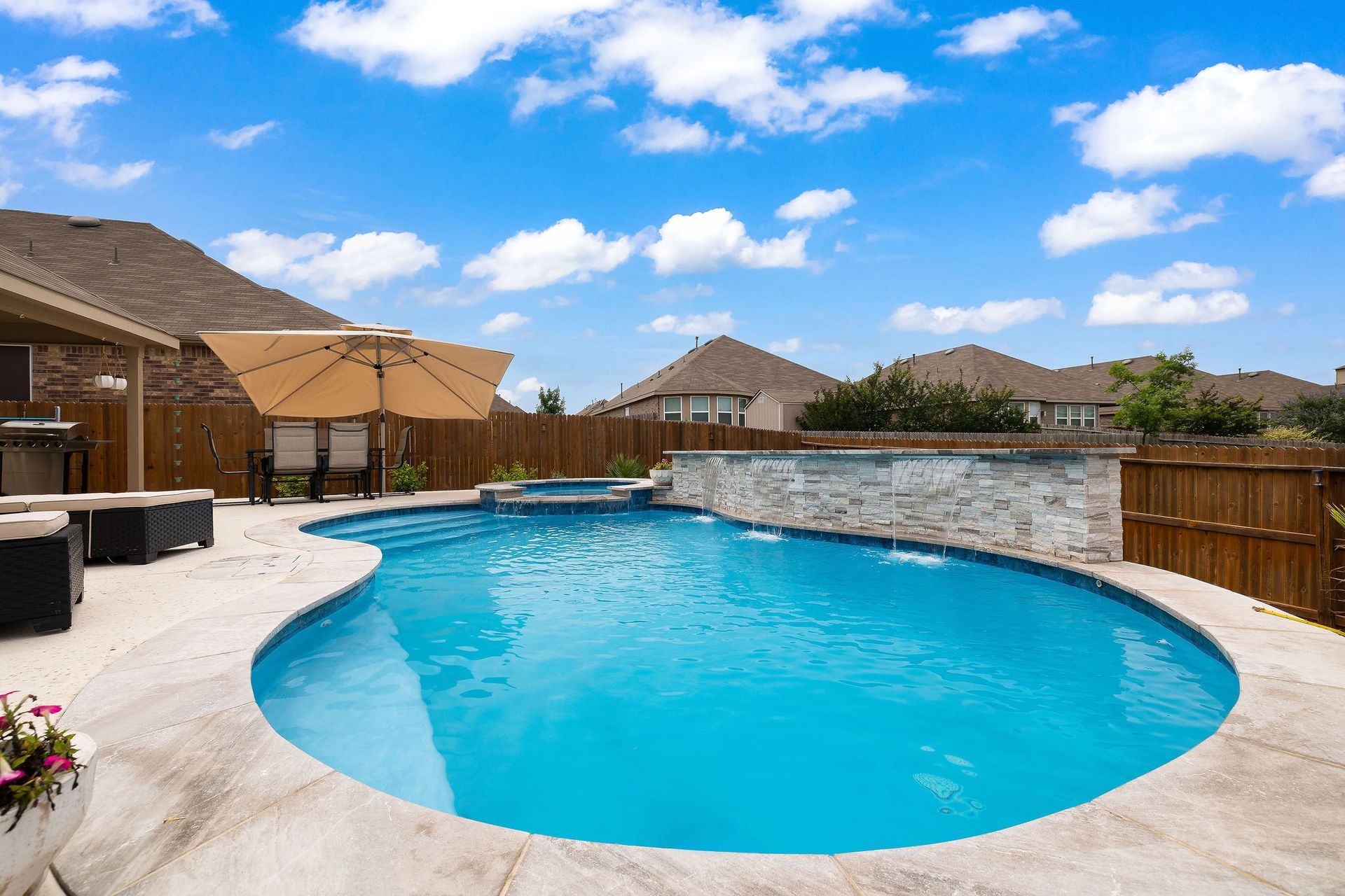 Backyard pool with spa, patio lounge chairs, and desert-style homes under a bright blue sky