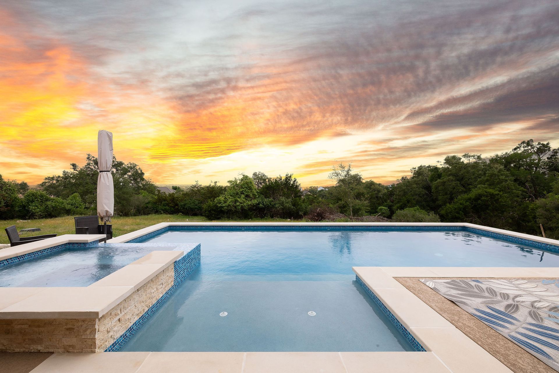 Infinity pool at sunset with a colorful sky and lush greenery beyond