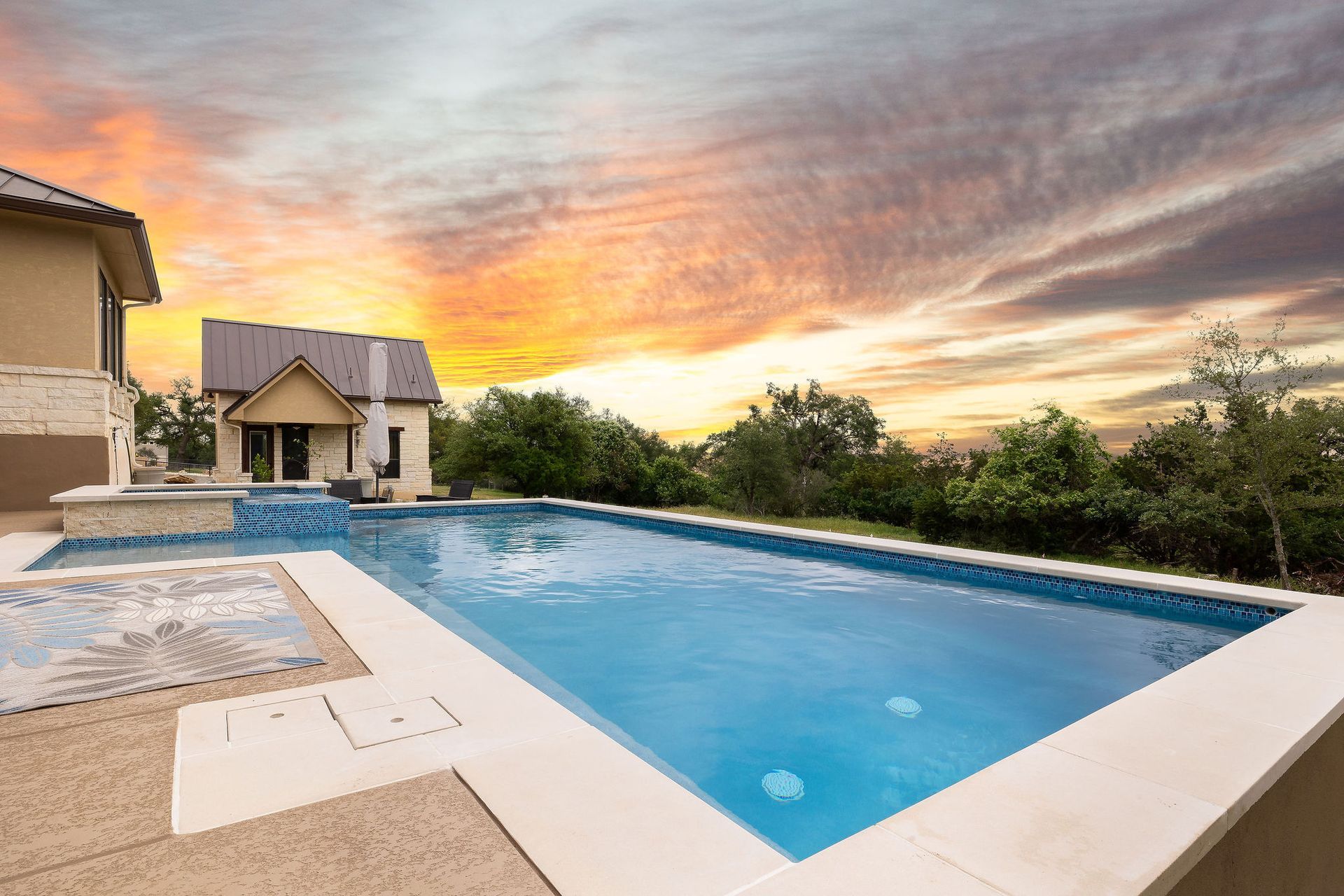 Backyard swimming pool at sunset beside a modern house with a dramatic orange sky
