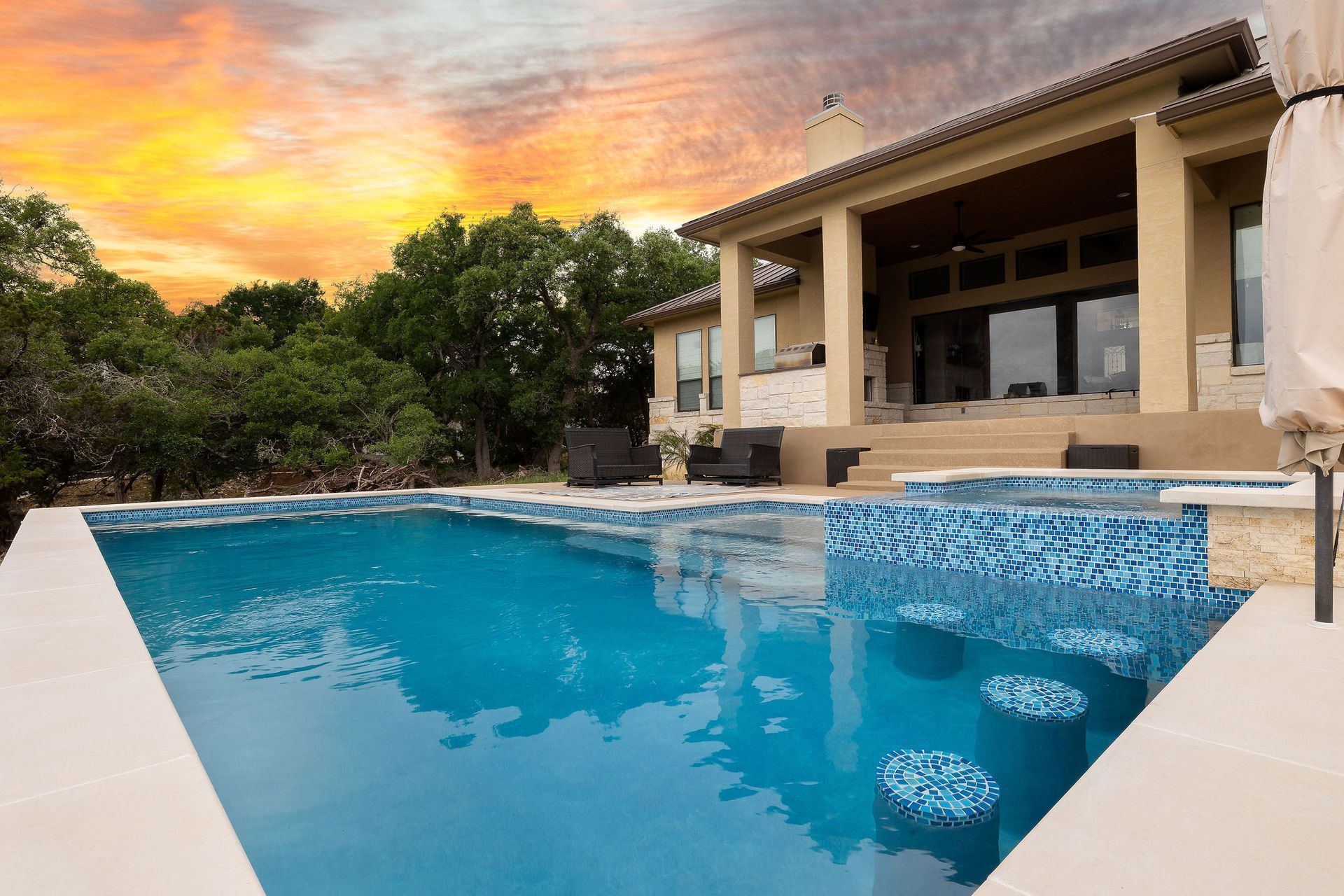 Luxury backyard pool at sunset beside a modern house with a blue mosaic water feature