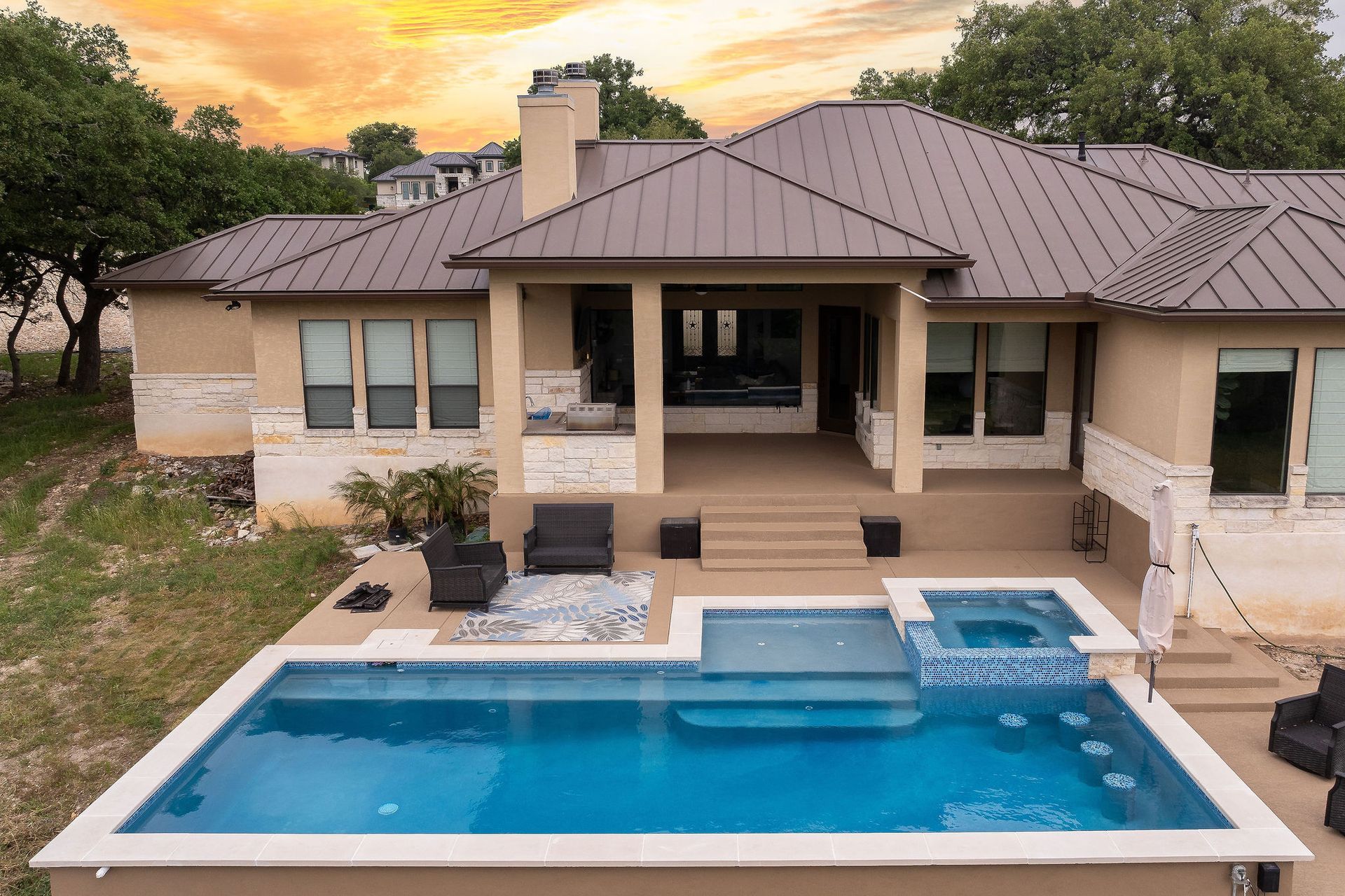 Backyard house with a covered patio and a rectangular swimming pool at sunset