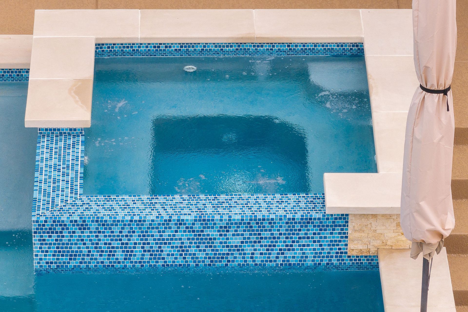 Blue tiled swimming pool with built-in steps and white lounge chairs at the edge