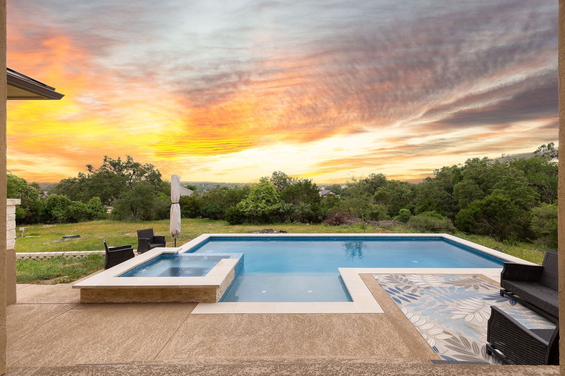 Backyard pool with spa at sunset, surrounded by greenery and patio seating