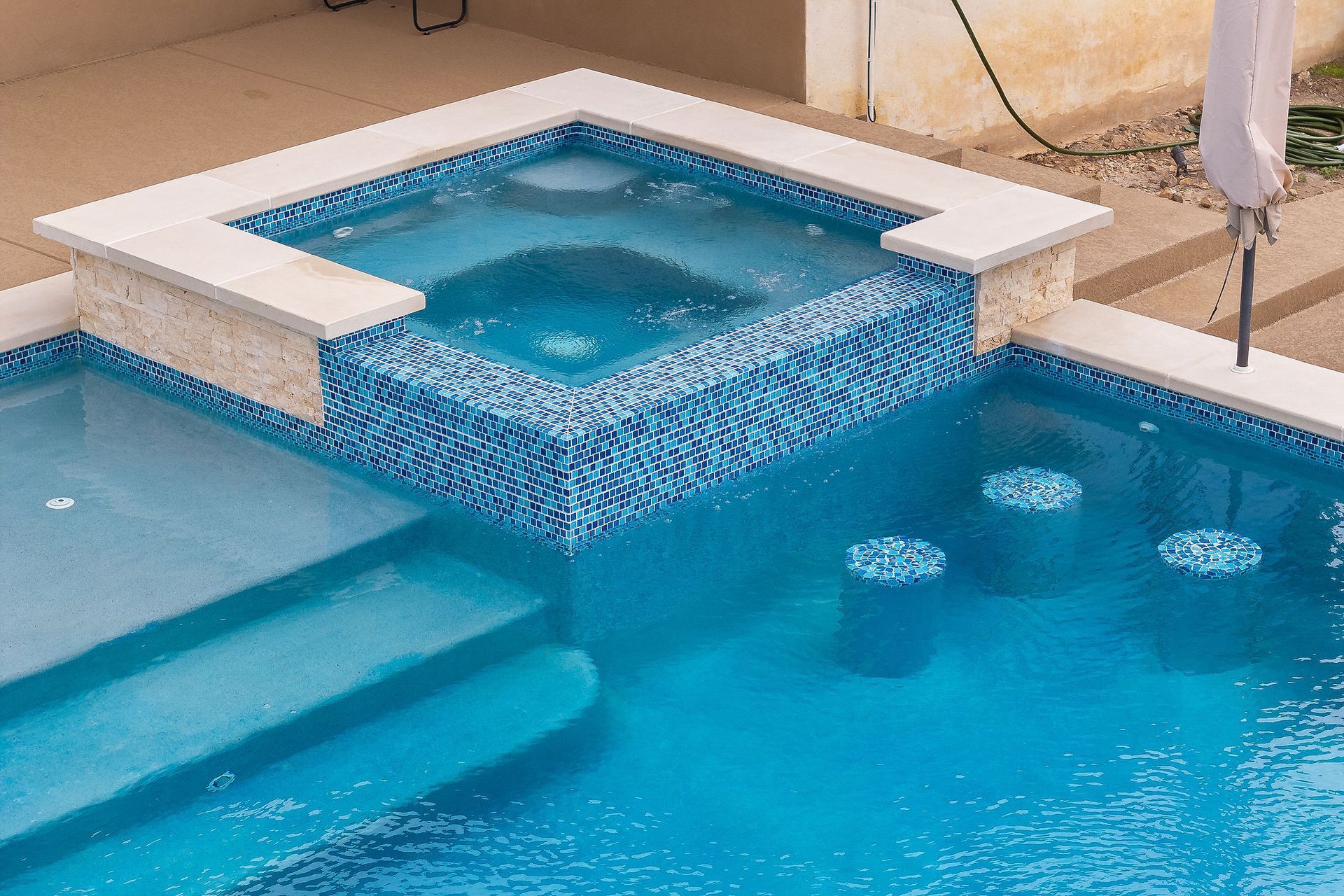 Blue swimming pool with raised square spa and tiled water feature overlook