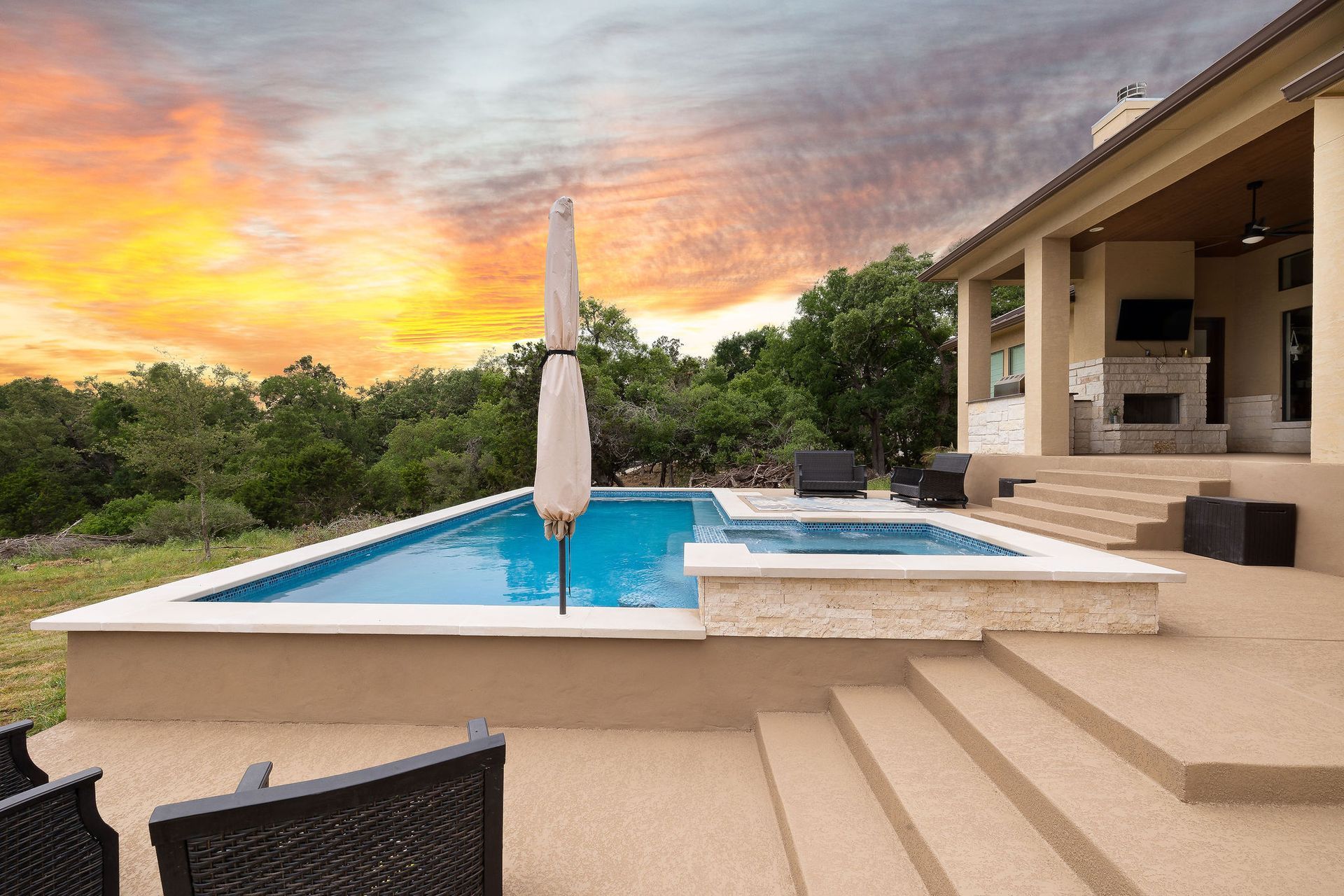 Backyard pool at sunset with patio steps, lounge chair, and a covered outdoor seating area