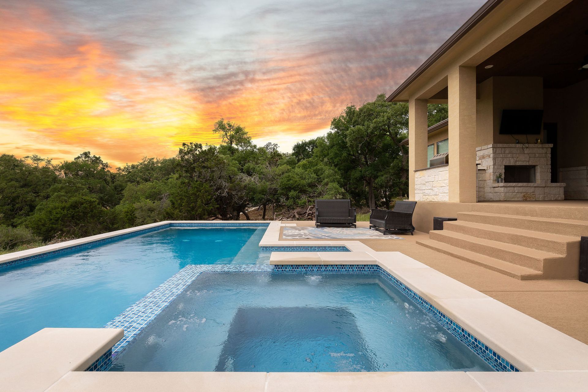 Luxury patio with infinity pool and hot tub at sunset, overlooking lush greenery