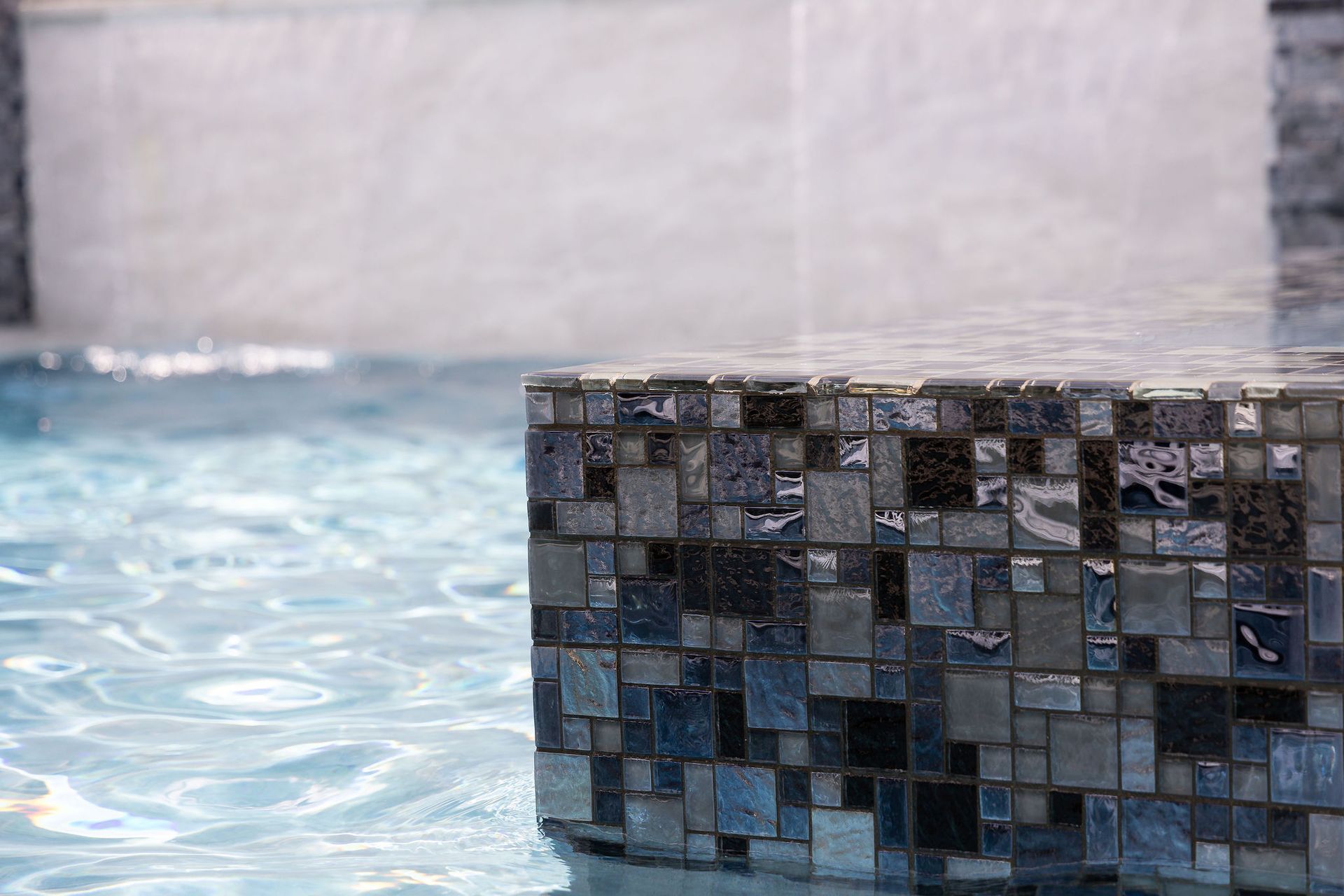 Blue-tiled fountain edge beside rippling water and a pale stone wall