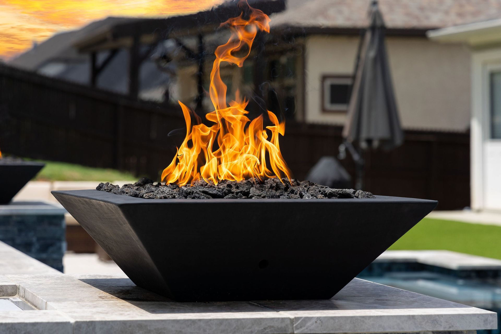 Black fire bowl with flames on a patio, with a house and backyard in the background