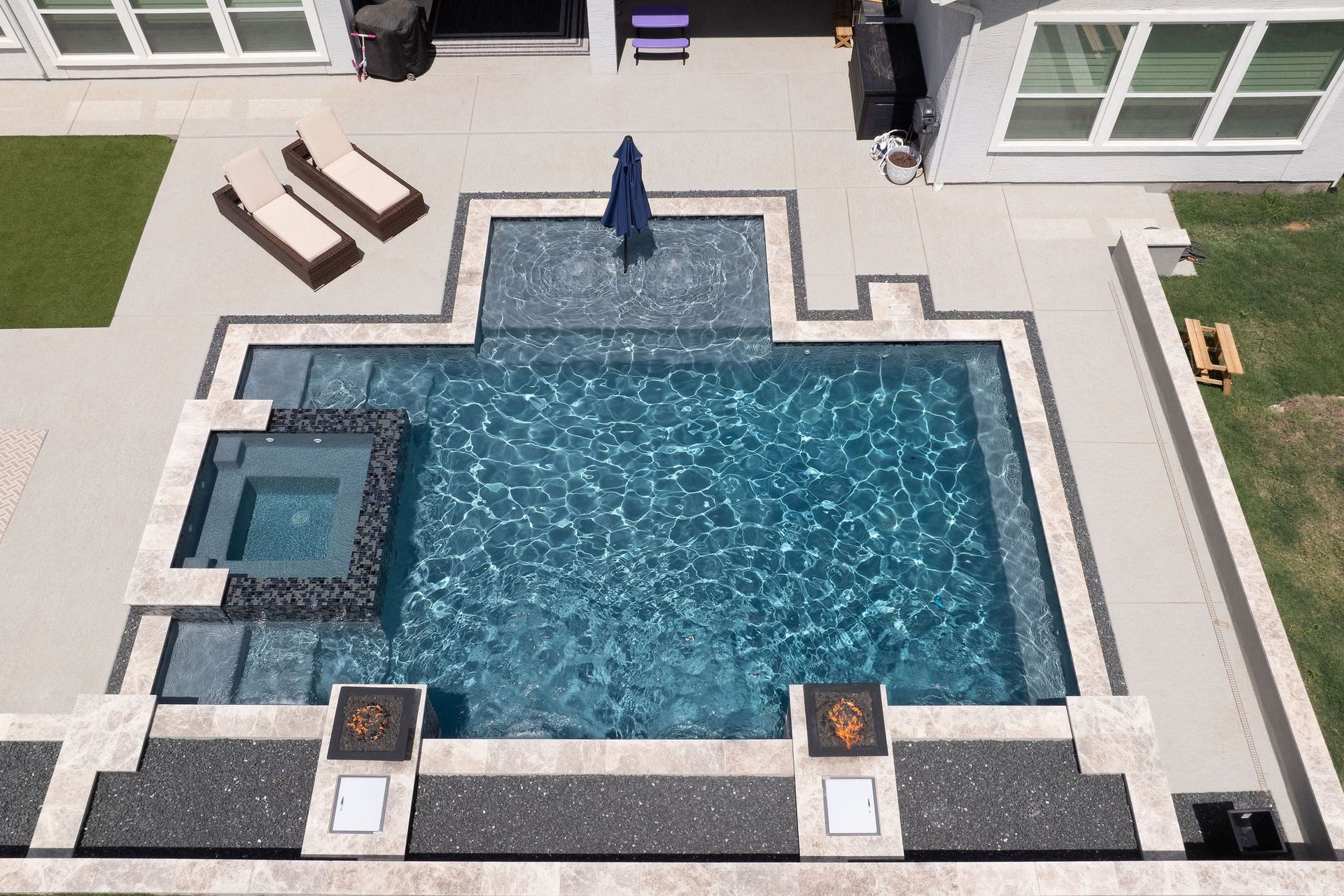 Overhead view of a backyard pool with blue water, spa, patio, lounge chairs, and a closed umbrella