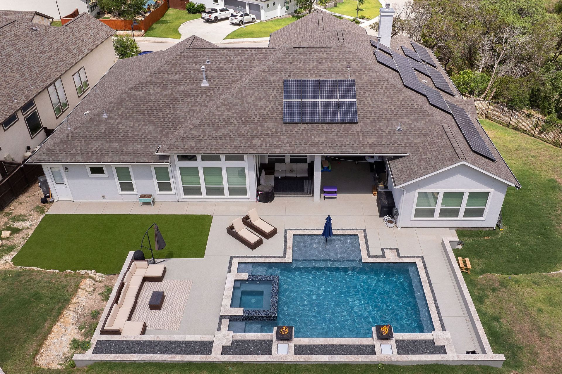 Overhead view of a backyard pool with blue water, spa, patio, lounge chairs, and a closed umbrella