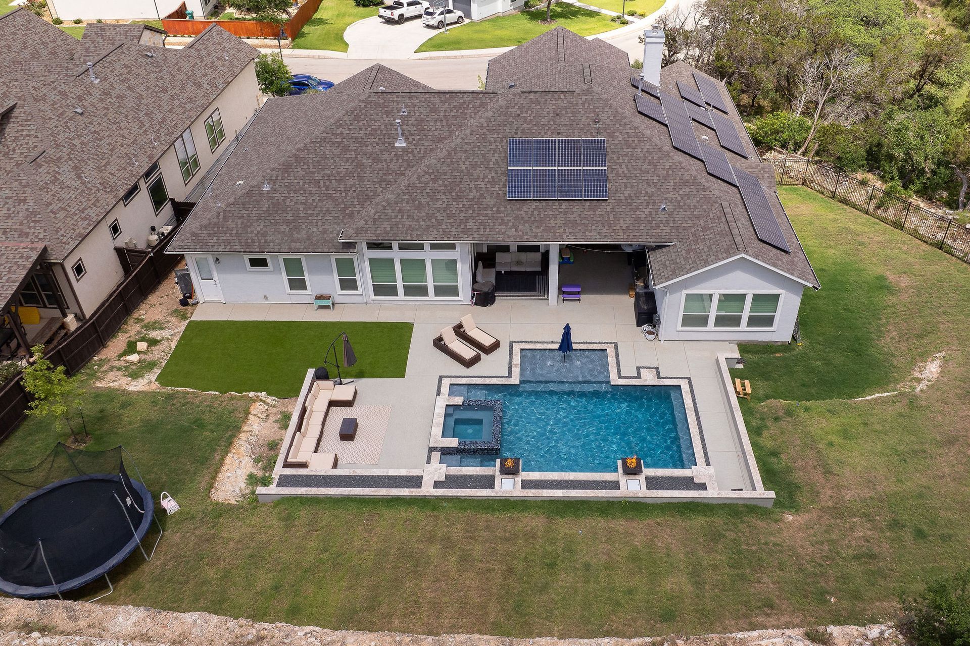 Overhead view of a backyard pool with blue water, spa, patio, lounge chairs, and a closed umbrella