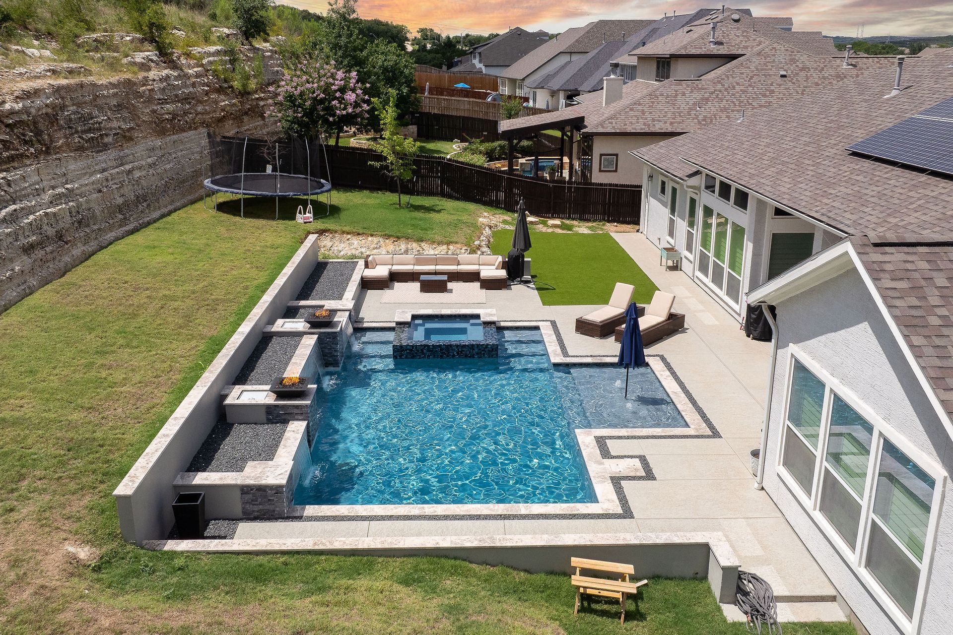 Overhead view of a backyard pool with blue water, spa, patio, lounge chairs, and a closed umbrella