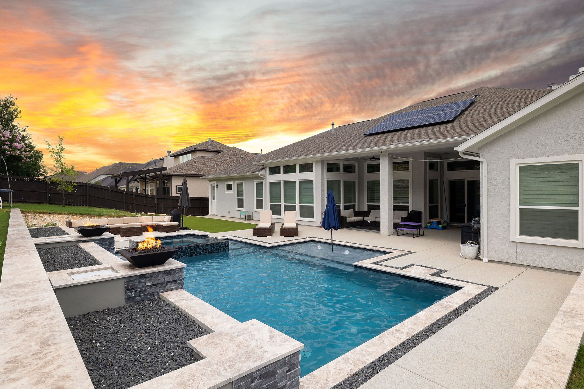 Backyard pool with lounge chairs, umbrella, and sunset sky behind a stone wall
