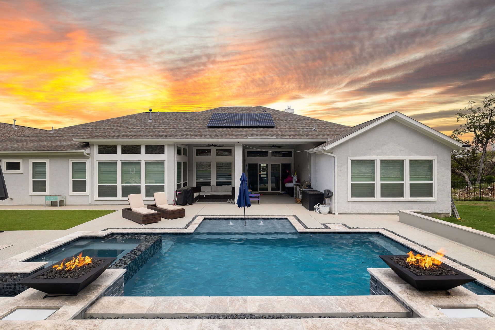 Backyard pool with lounge chairs, umbrella, and sunset sky behind a stone wall