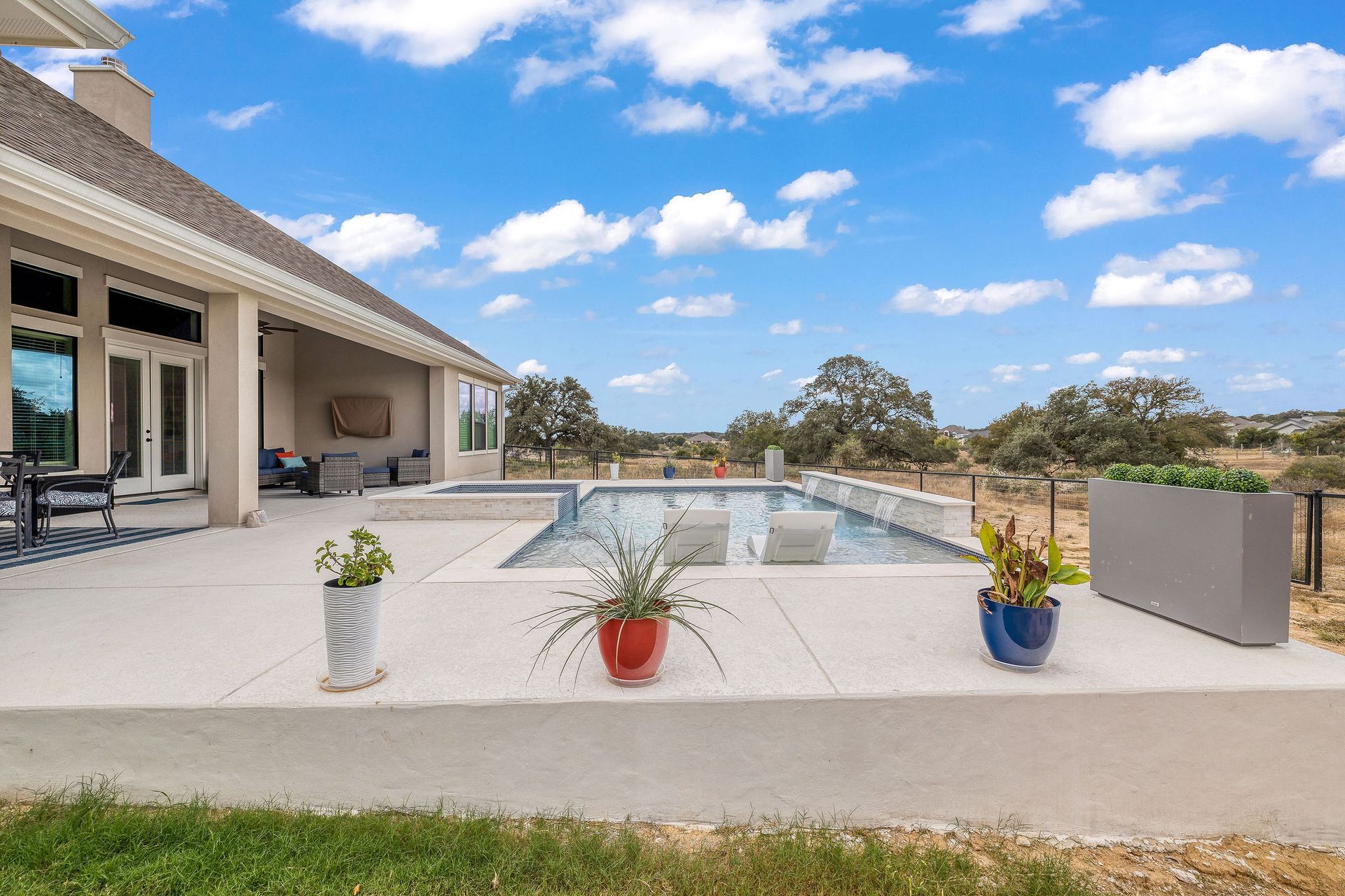 Backyard patio with a rectangular pool, potted plants, and a cloudy blue sky