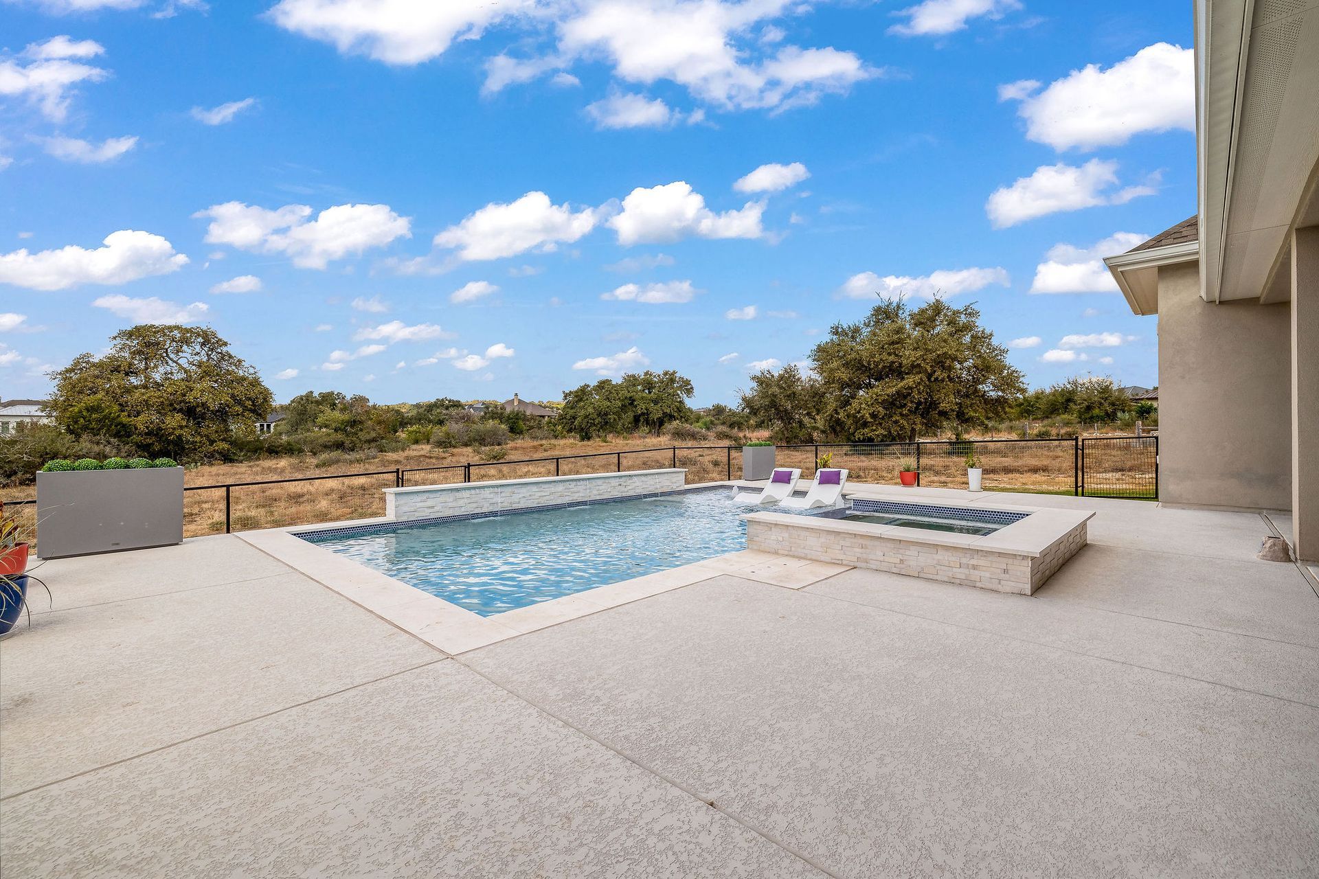 Modern patio with a blue pool, lounge chairs, and open sky view