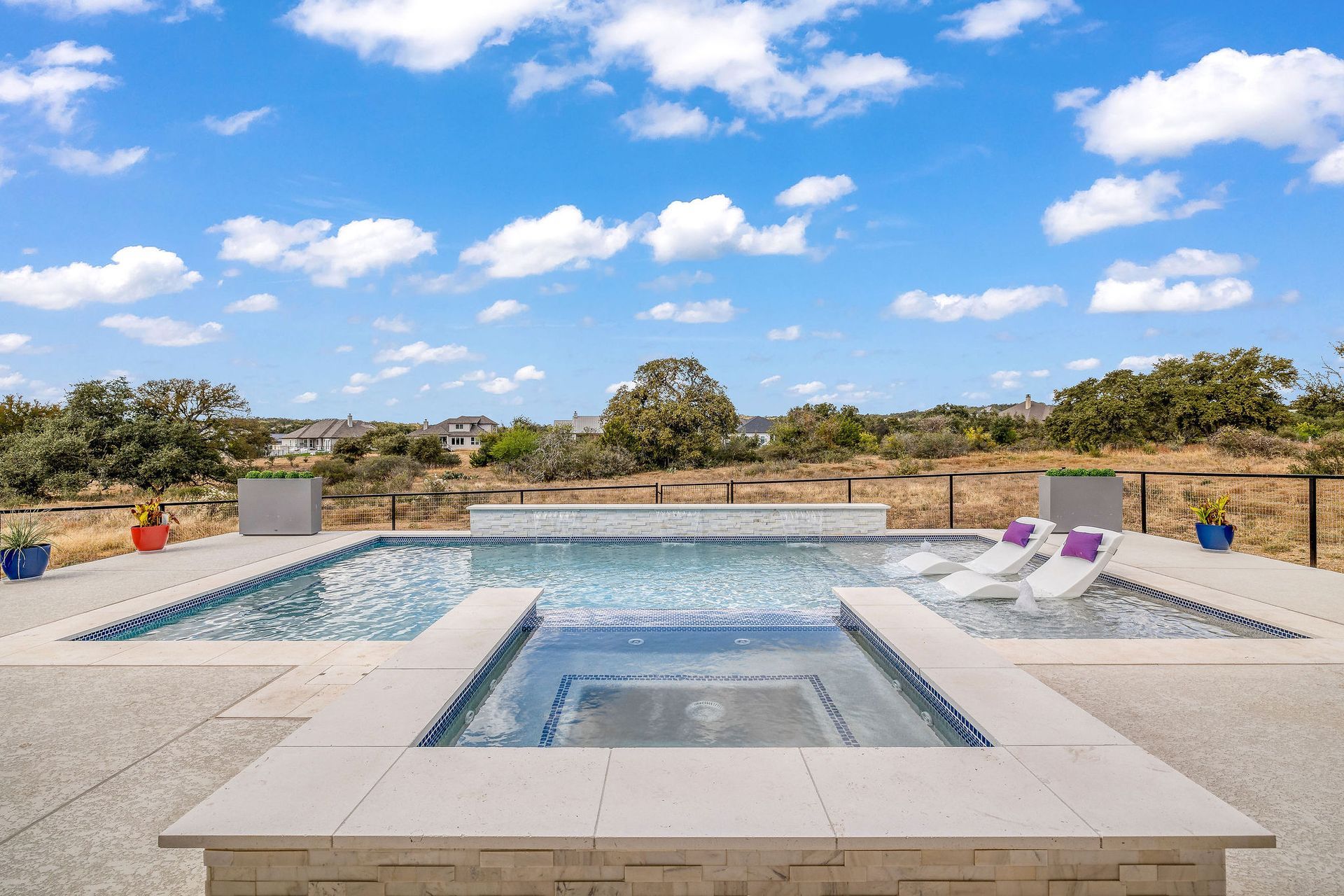 Modern patio with a blue pool, lounge chairs, and open sky view