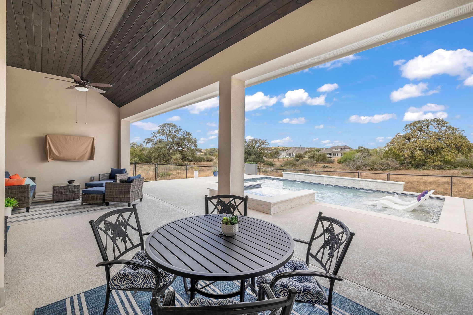 Patio with round table and chairs overlooking a pool and open landscape under a covered roof