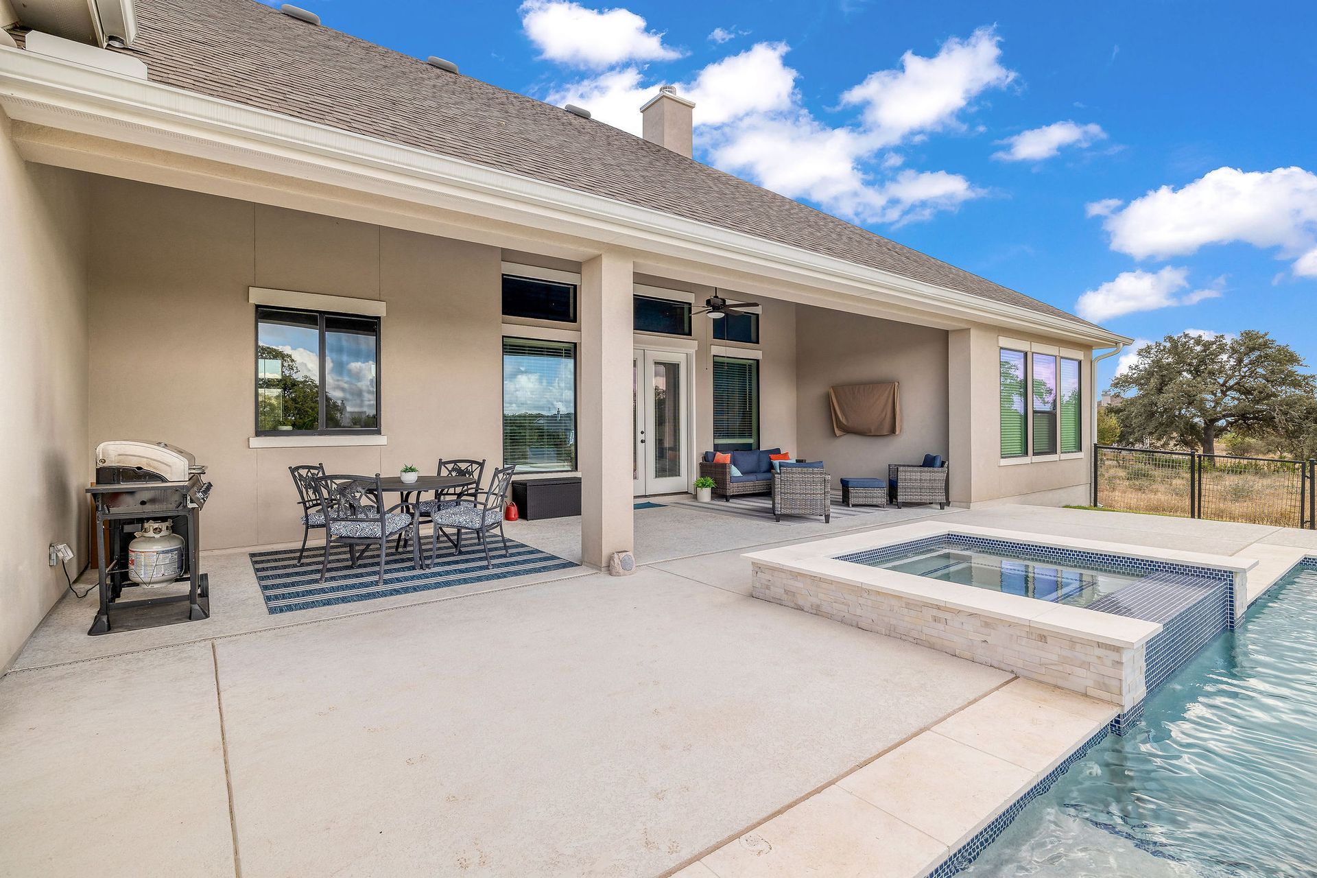 Patio with outdoor seating beside a pool and spa, under a covered backyard patio with blue sky