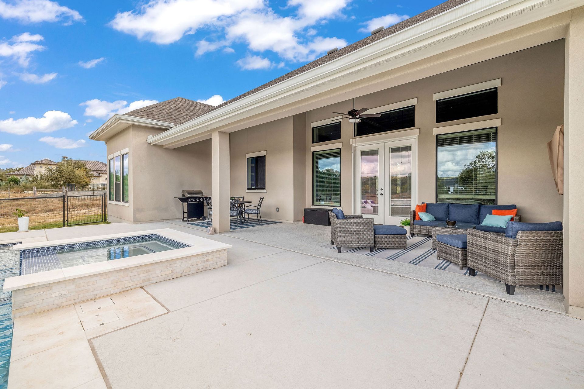 Spacious patio with outdoor seating, sliding glass doors, and a small pool under a partly cloudy sky