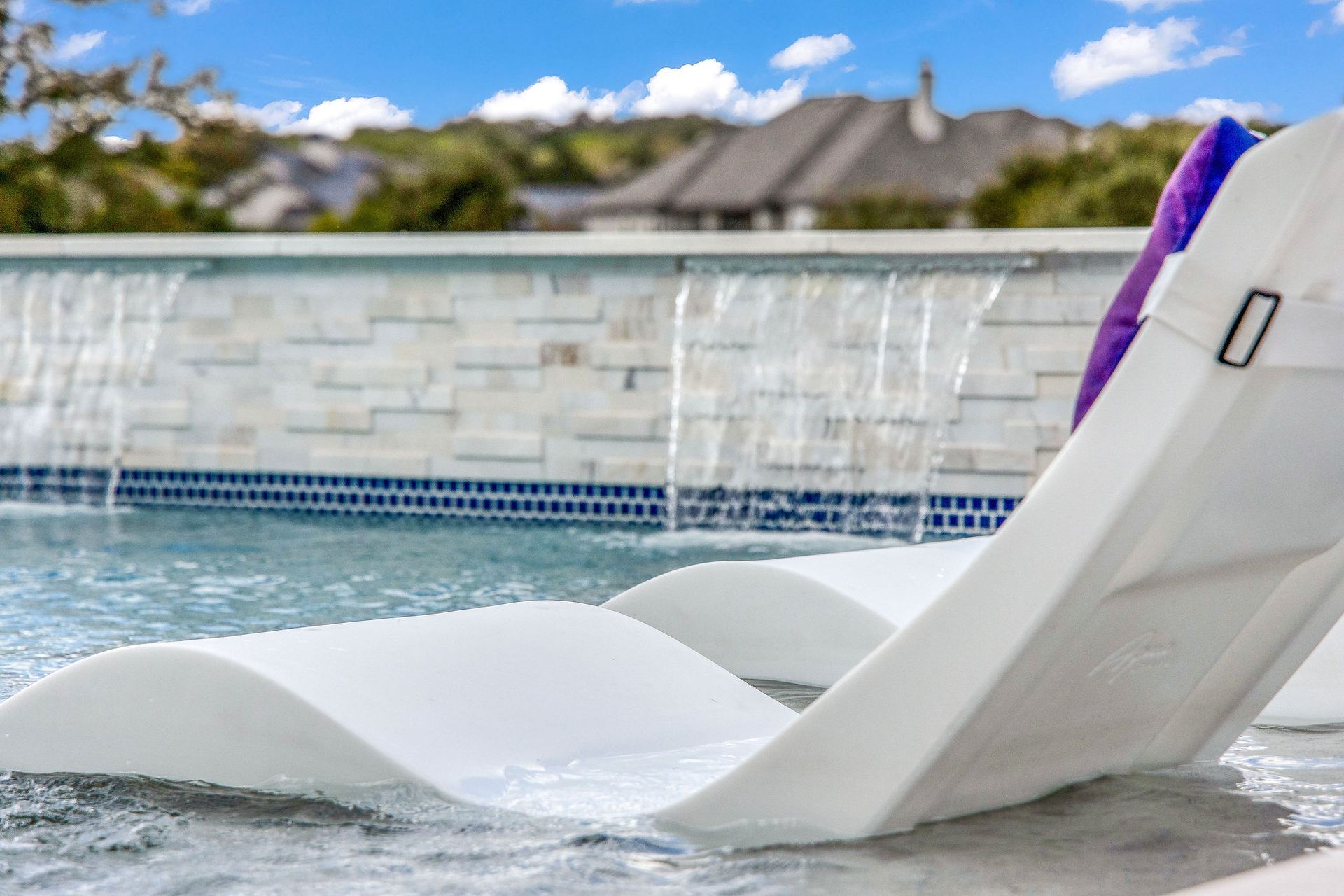 White lounge chair at a poolside with water spraying in the background