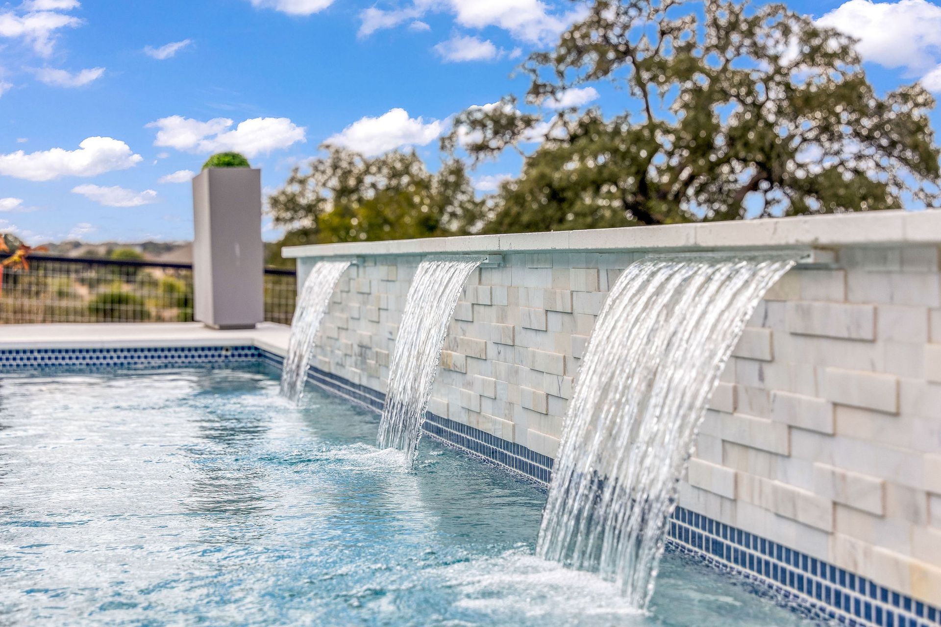 Modern pool with cascading water fountains and blue tile edge under a sunny sky