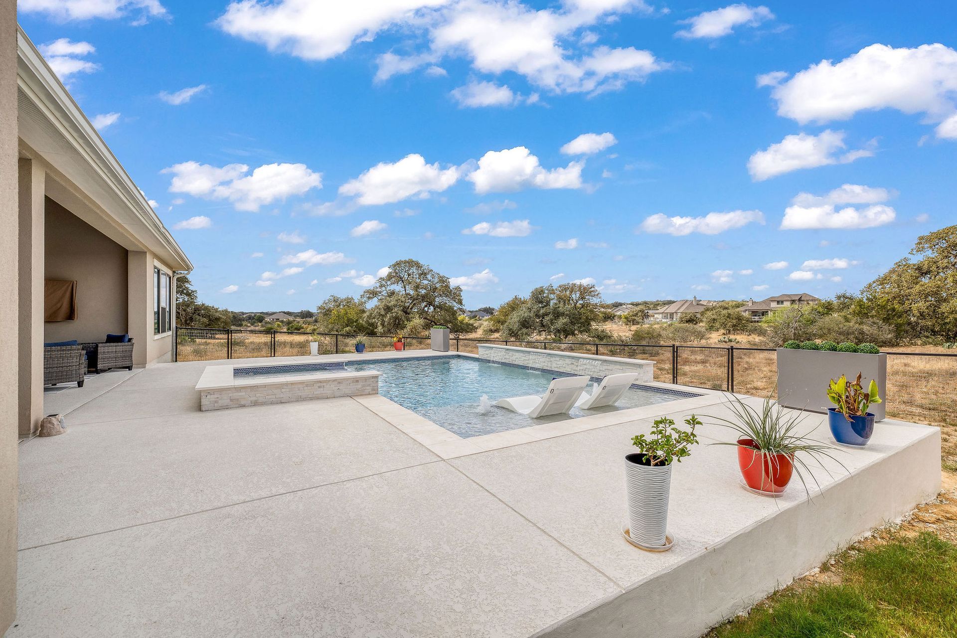 Patio with white concrete, small pool, potted flowers, and a bright blue sky with clouds