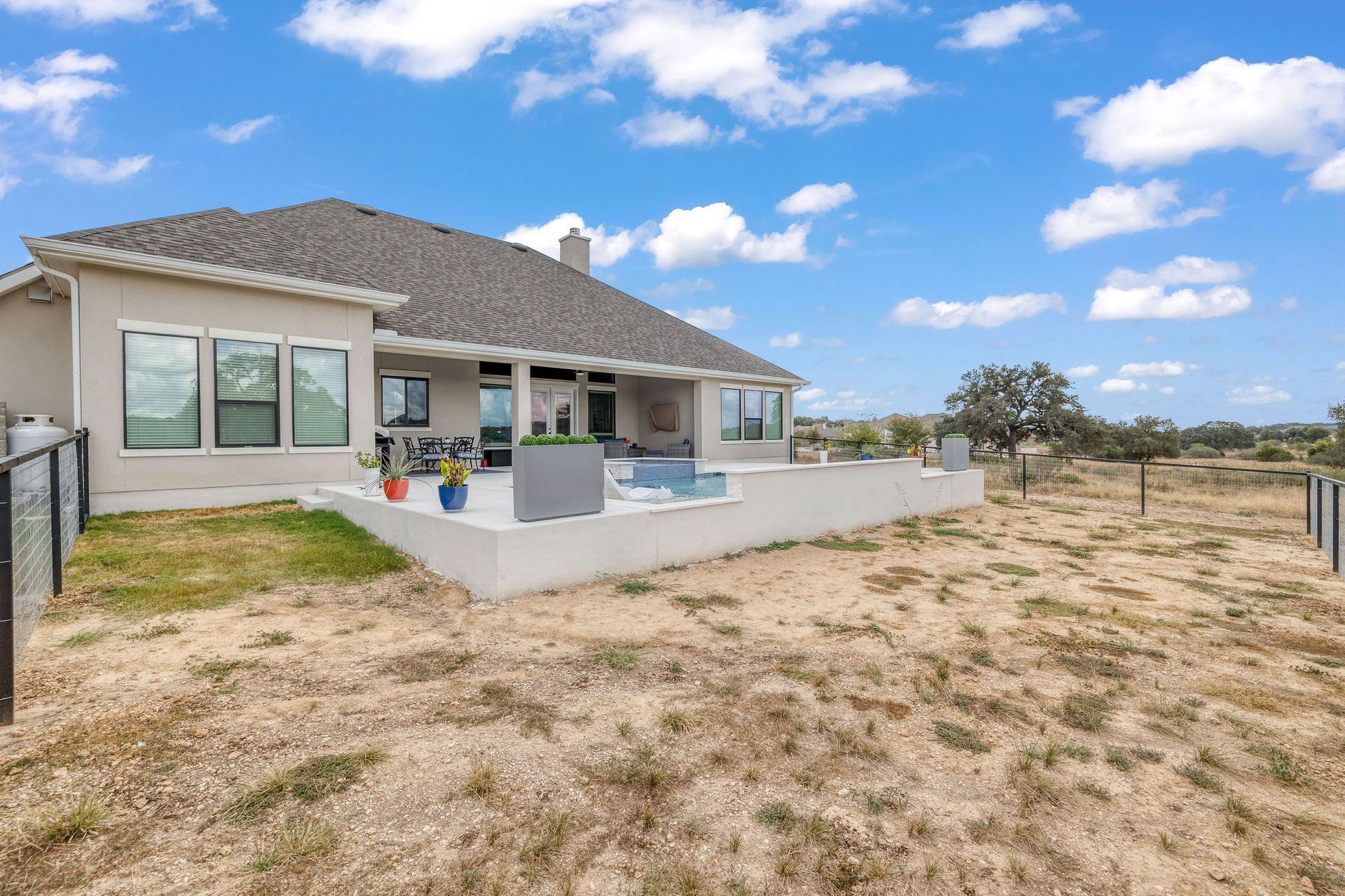 Modern house with a covered patio and fenced yard on a grassy lot under a blue sky