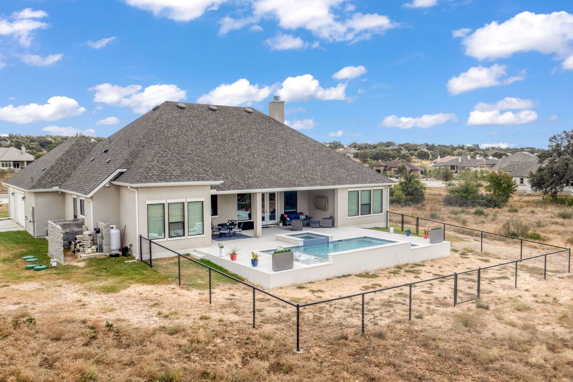 Single-story house with a backyard pool, patio, and fenced yard under a bright blue sky