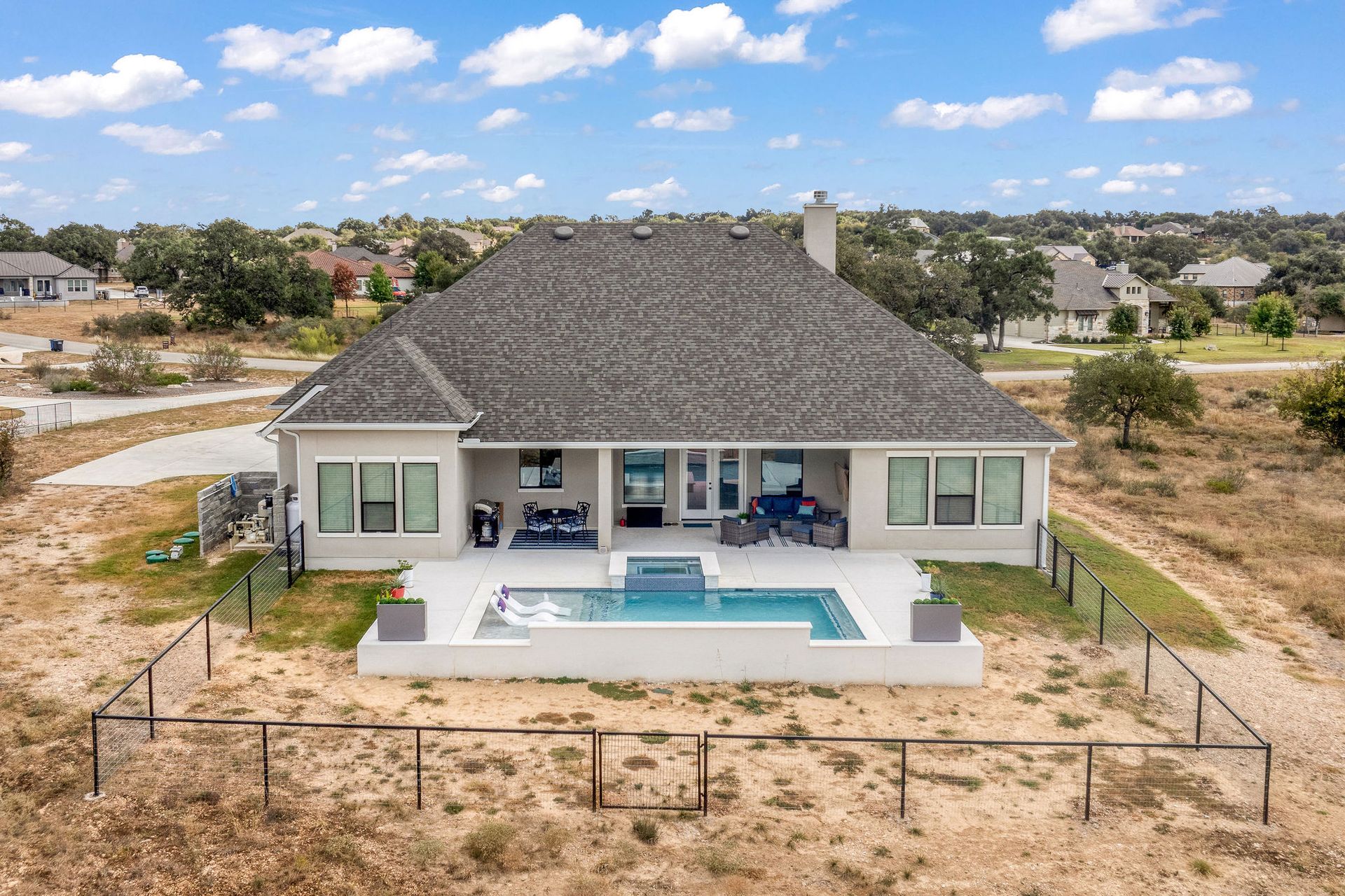 Aerial view of a modern house with a backyard pool and patio in a dry suburban neighborhood