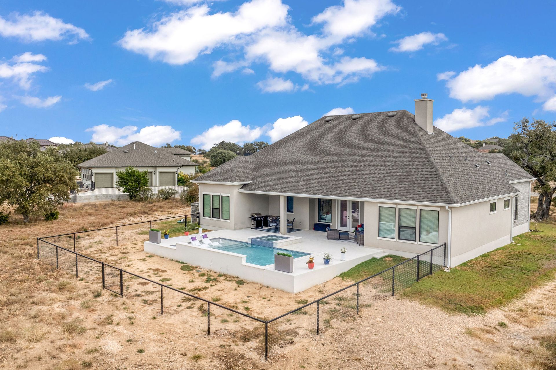 Modern white house with a gray roof, patio, and fenced yard under a blue sky