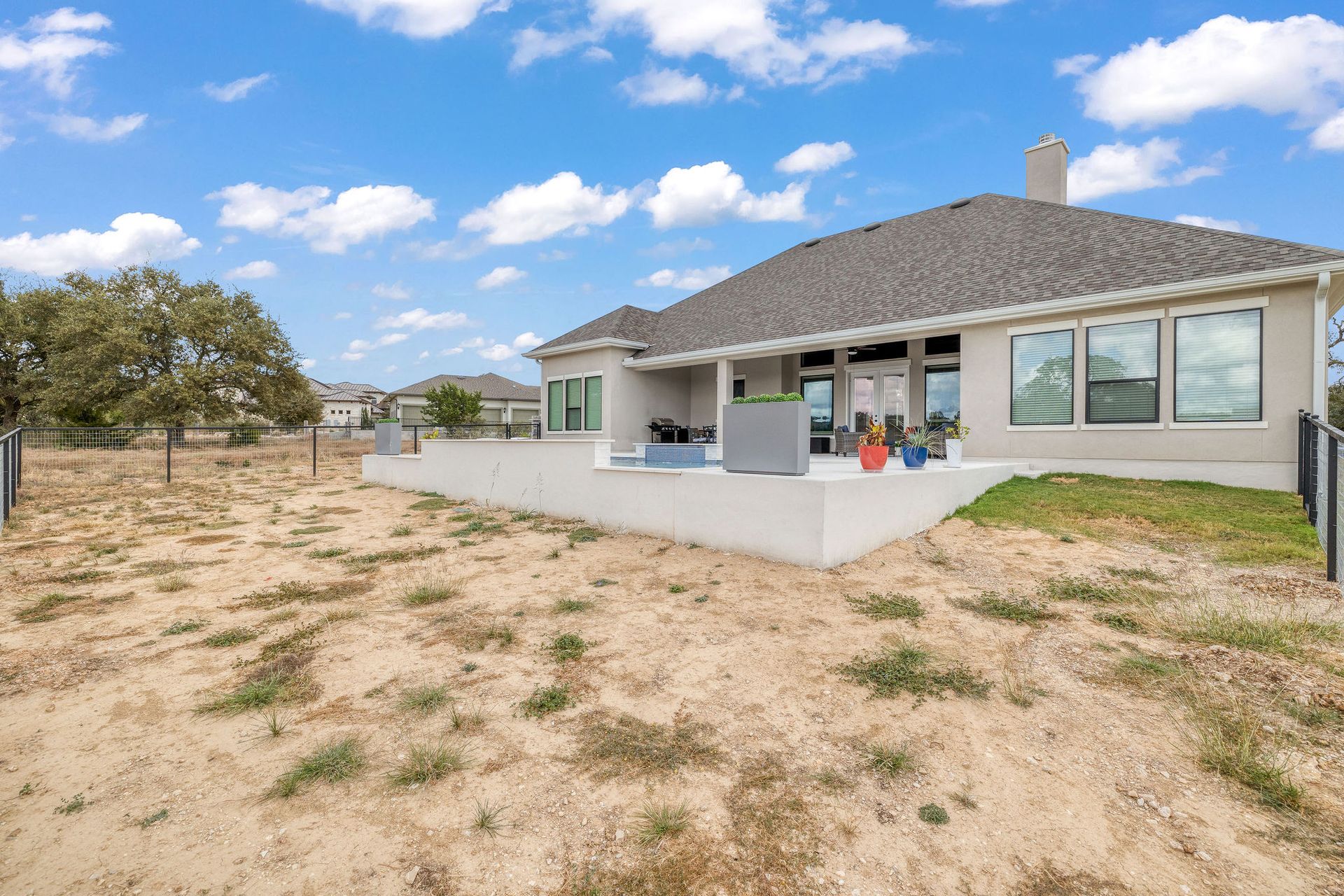 Modern single-story house with a covered patio and dry, grassy yard under a partly cloudy sky