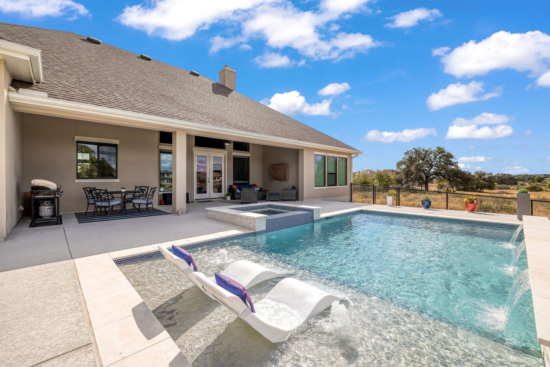 Backyard pool beside a covered patio with lounge chairs under a bright blue sky